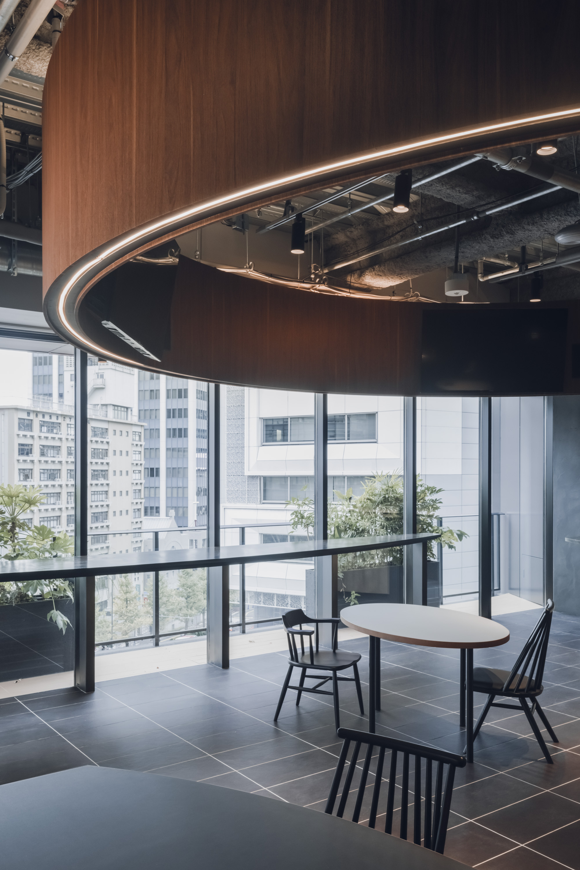 Detail of the sweeping wood canopy edge with concealed linear lighting beside full-height glazing and terrace planters