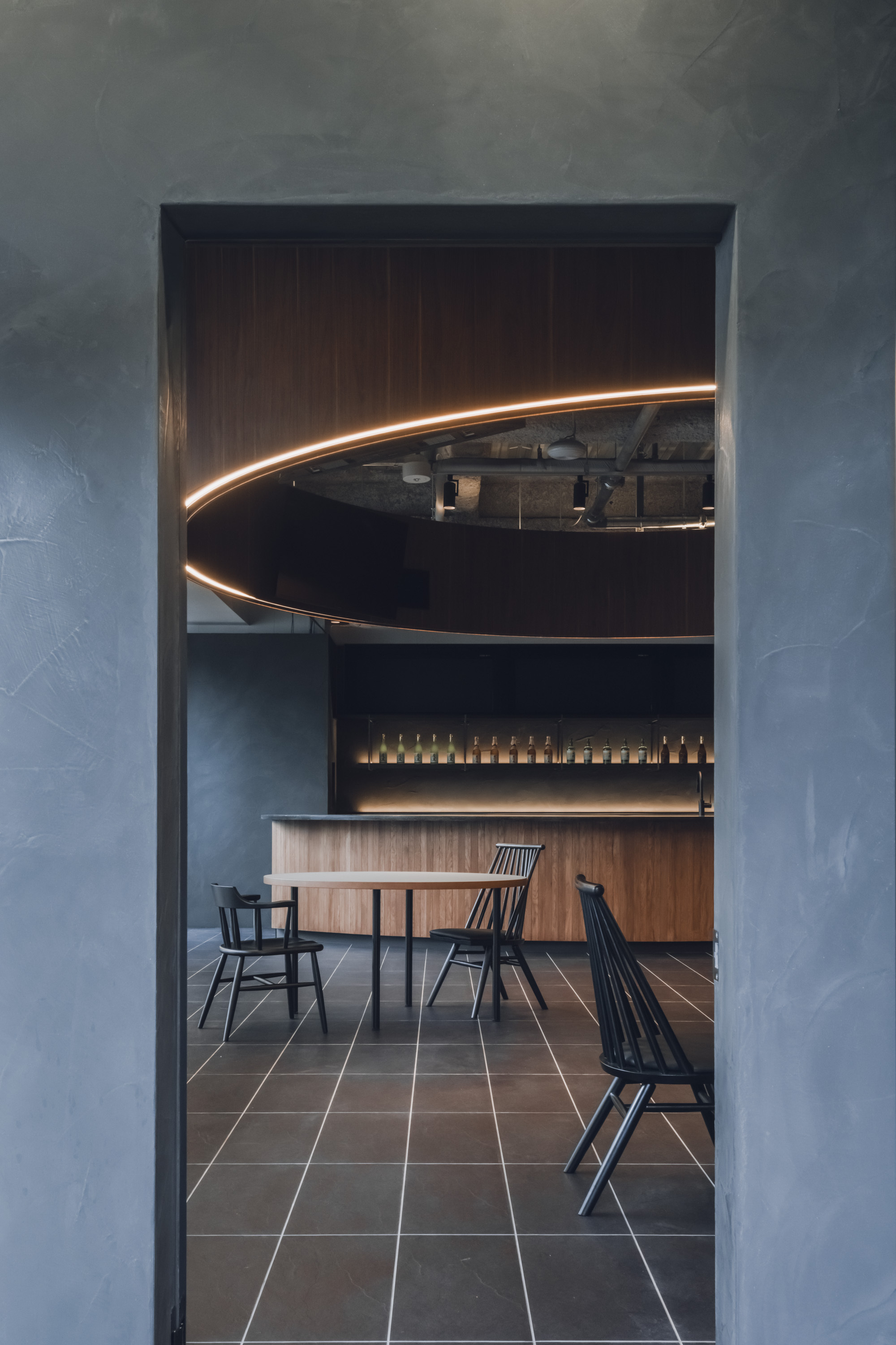 View through doorway framed by textured grey walls toward dining space with curved illuminated canopy overhead