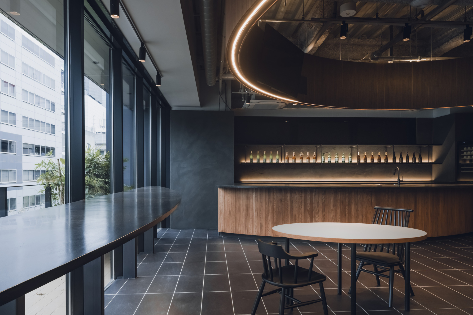 Office breakroom with floor-to-ceiling windows, walnut cabinetry, and circular LED light fixture above exposed mechanical ceiling