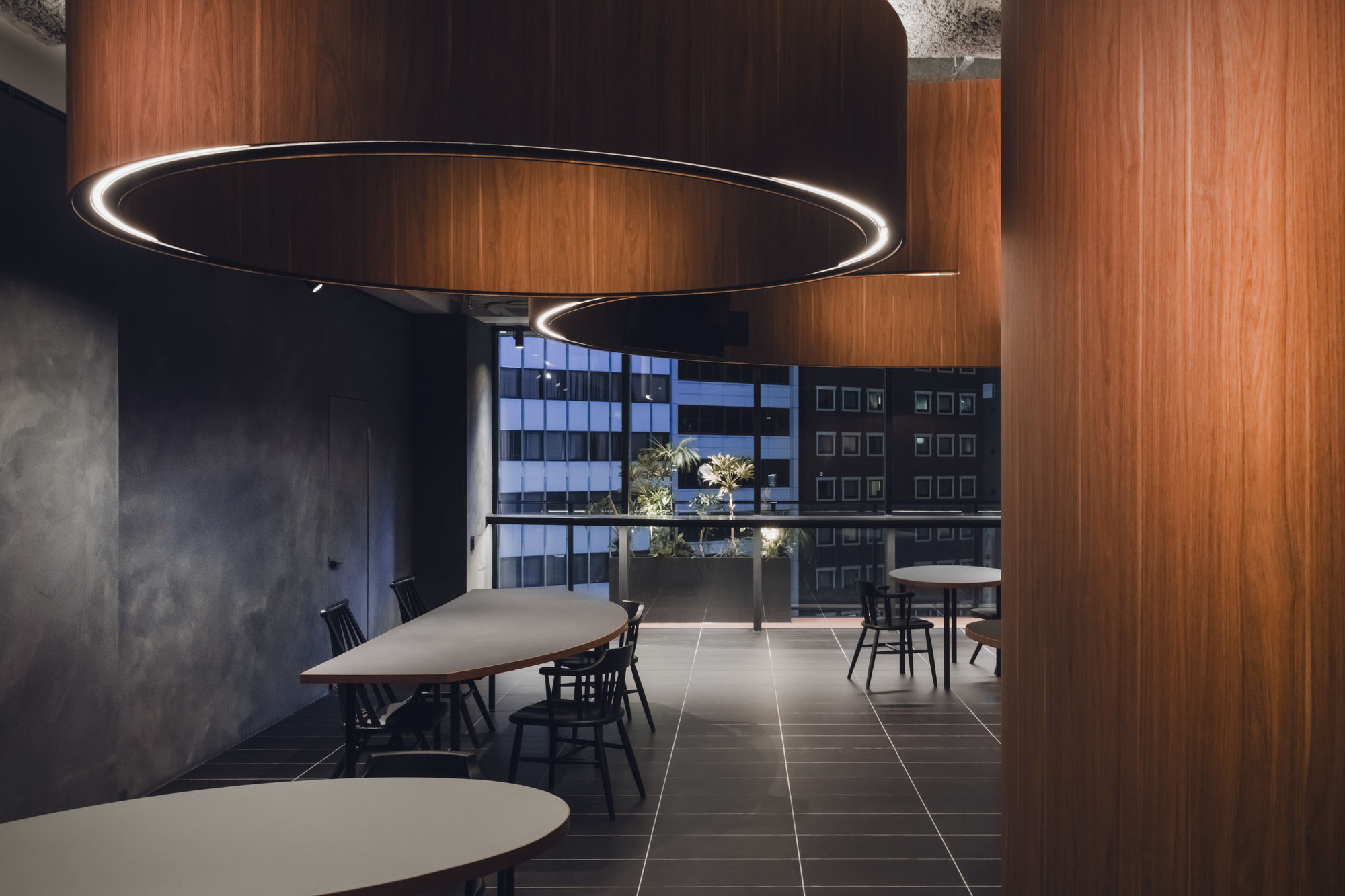 Curved timber partition walls framing window view toward adjacent office buildings with rooftop greenery visible
