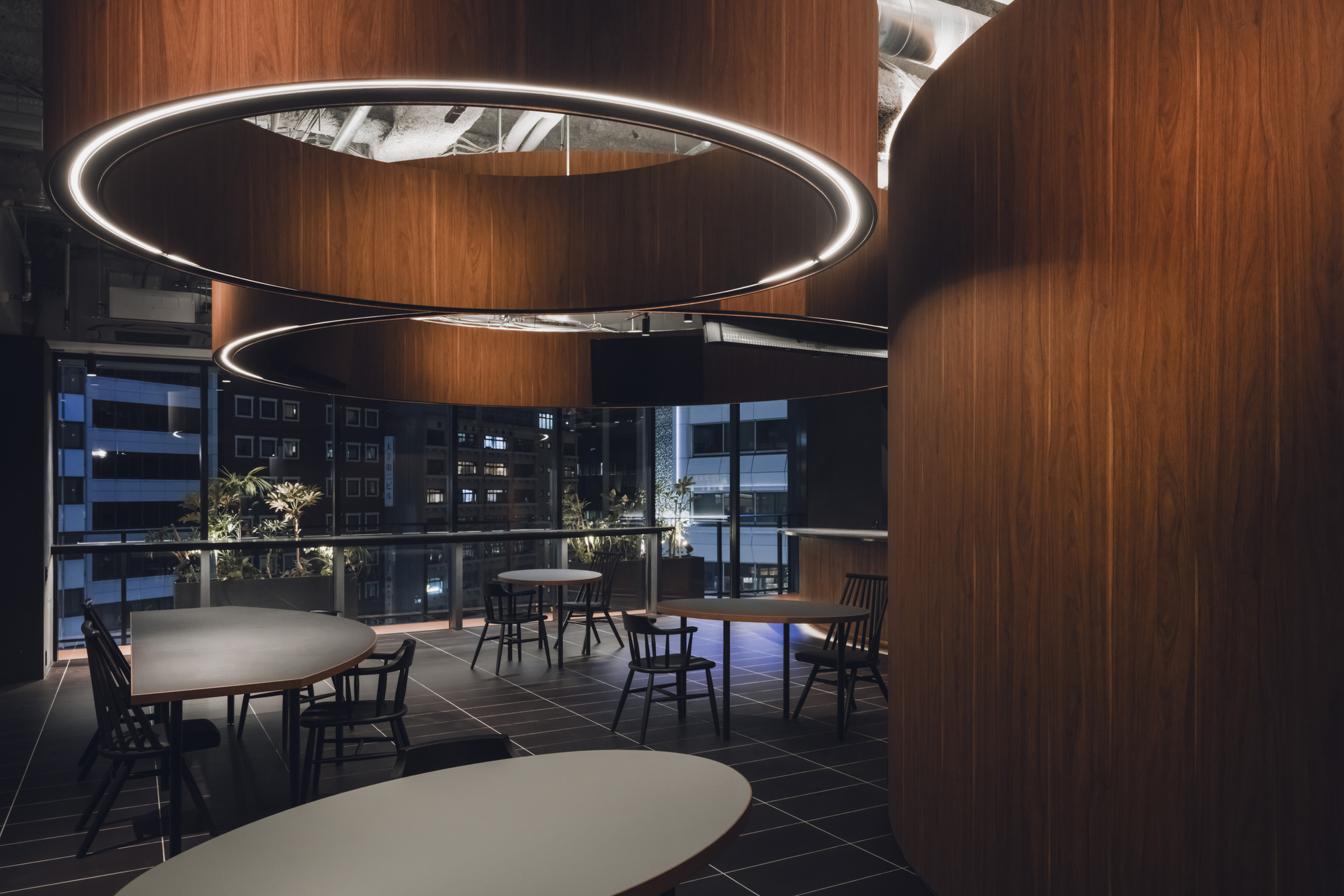 Evening view of dining area showing circular LED pendants and city lights through floor-to-ceiling glazing