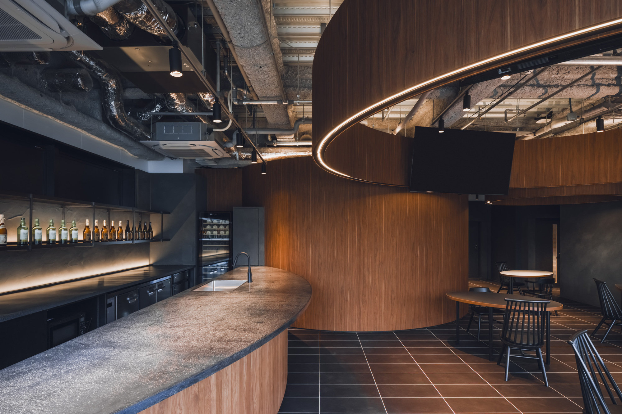 Curved service counter with terrazzo surface adjacent to walnut-clad volume under exposed ductwork and industrial ceiling