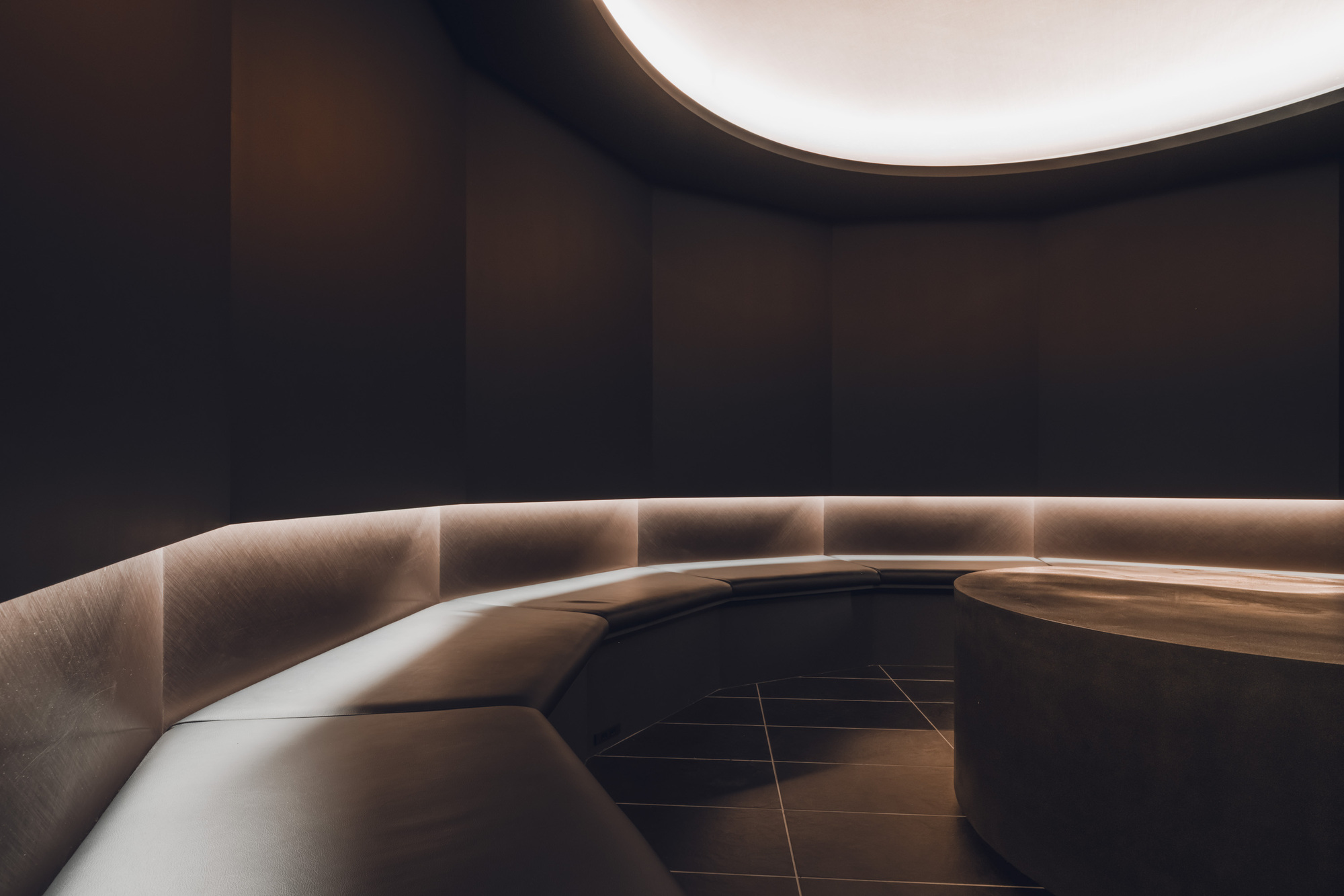 Curved bench with integrated strip lighting along its base against dark walls under a rounded ceiling