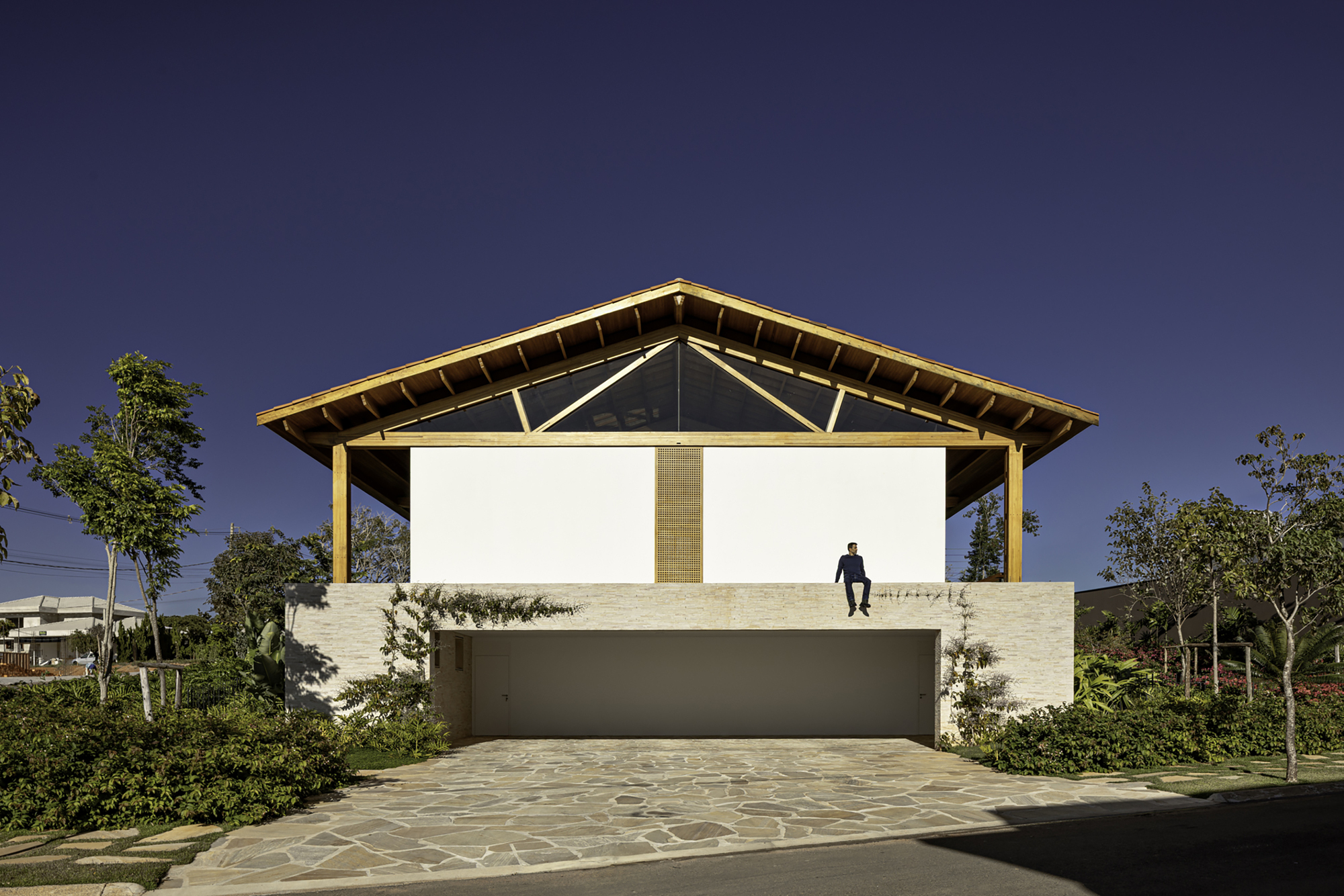 Street facade with exposed timber roof structure, white masonry base, and a figure standing on the upper terrace