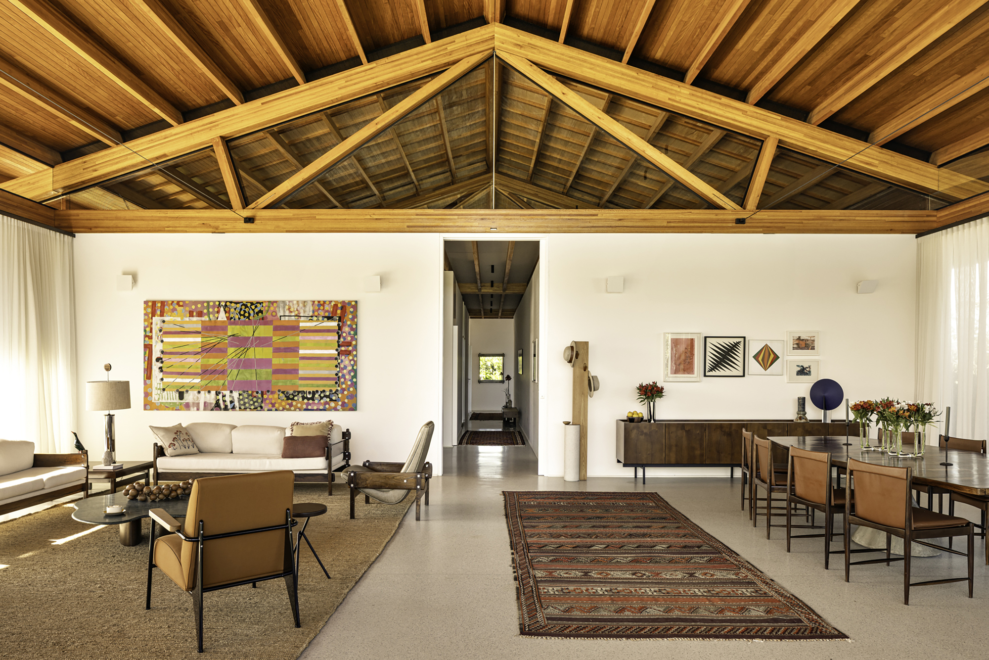 Open-plan living and dining space beneath exposed timber trusses and tongue-and-groove ceiling planks