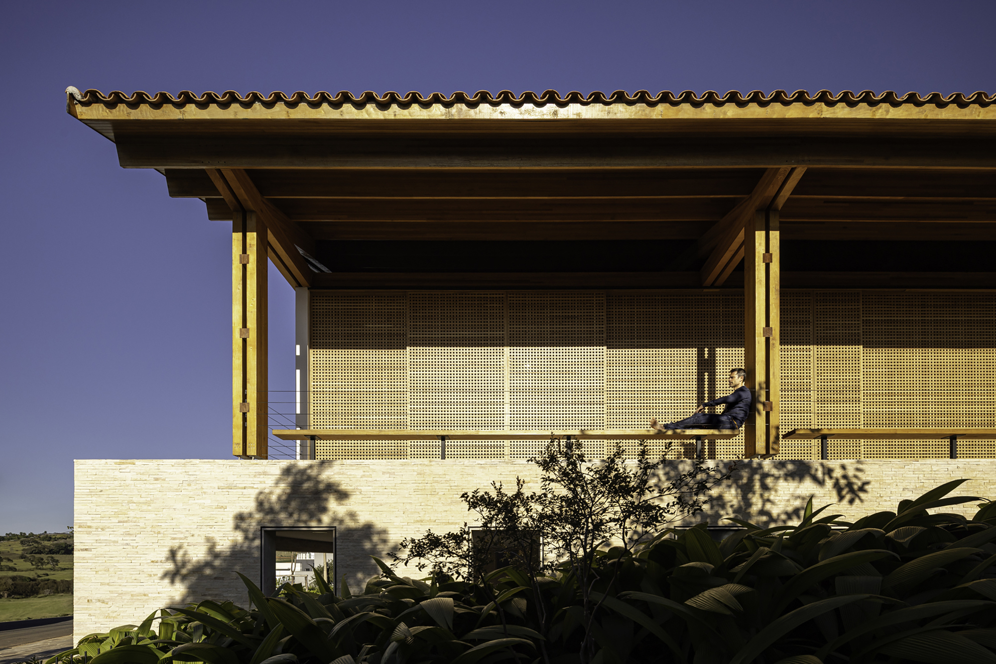 Upper terrace with perforated brick screen panels and timber roof soffit lit at dusk