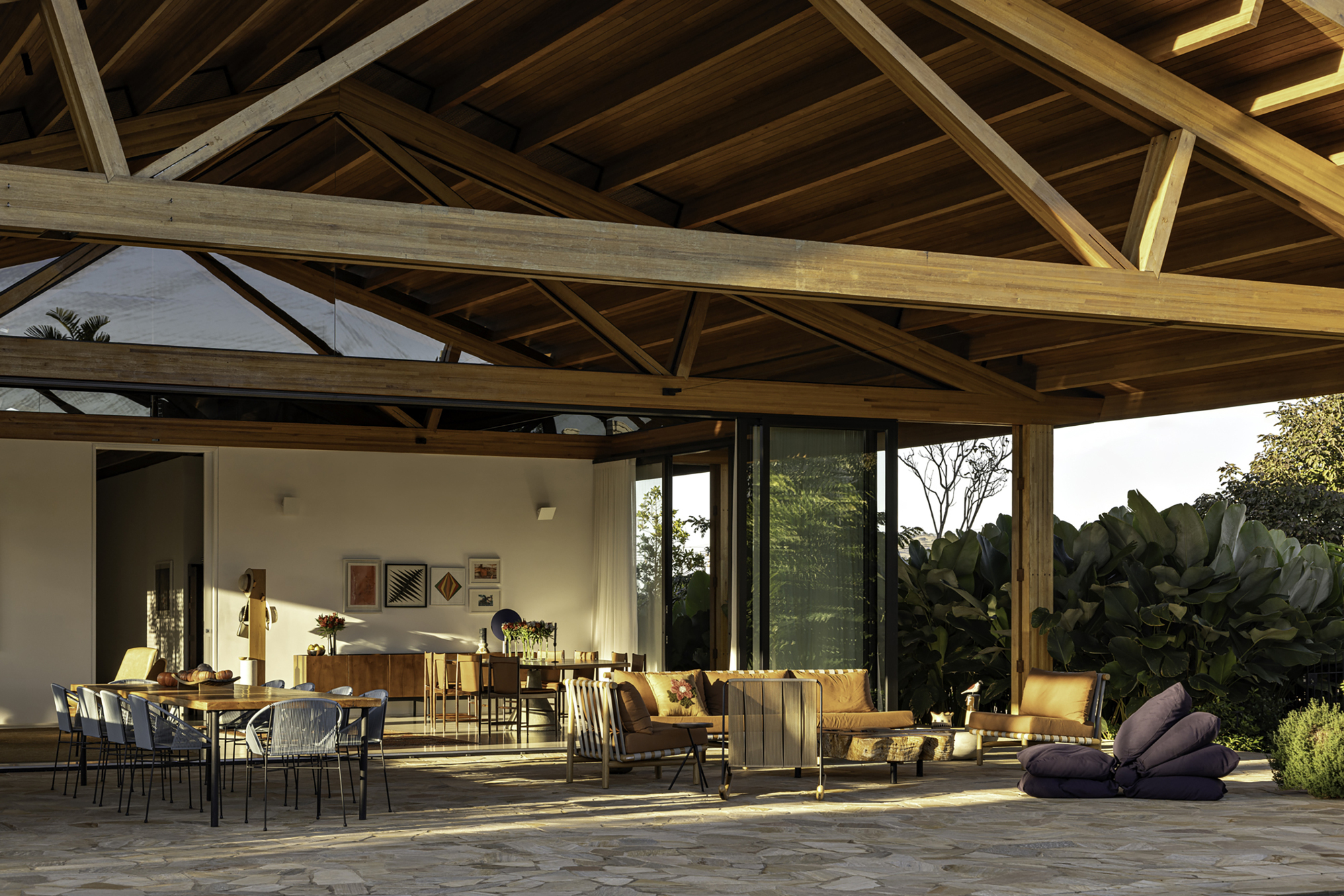 Covered outdoor terrace with stone paving and exposed timber trusses opening to lush tropical planting