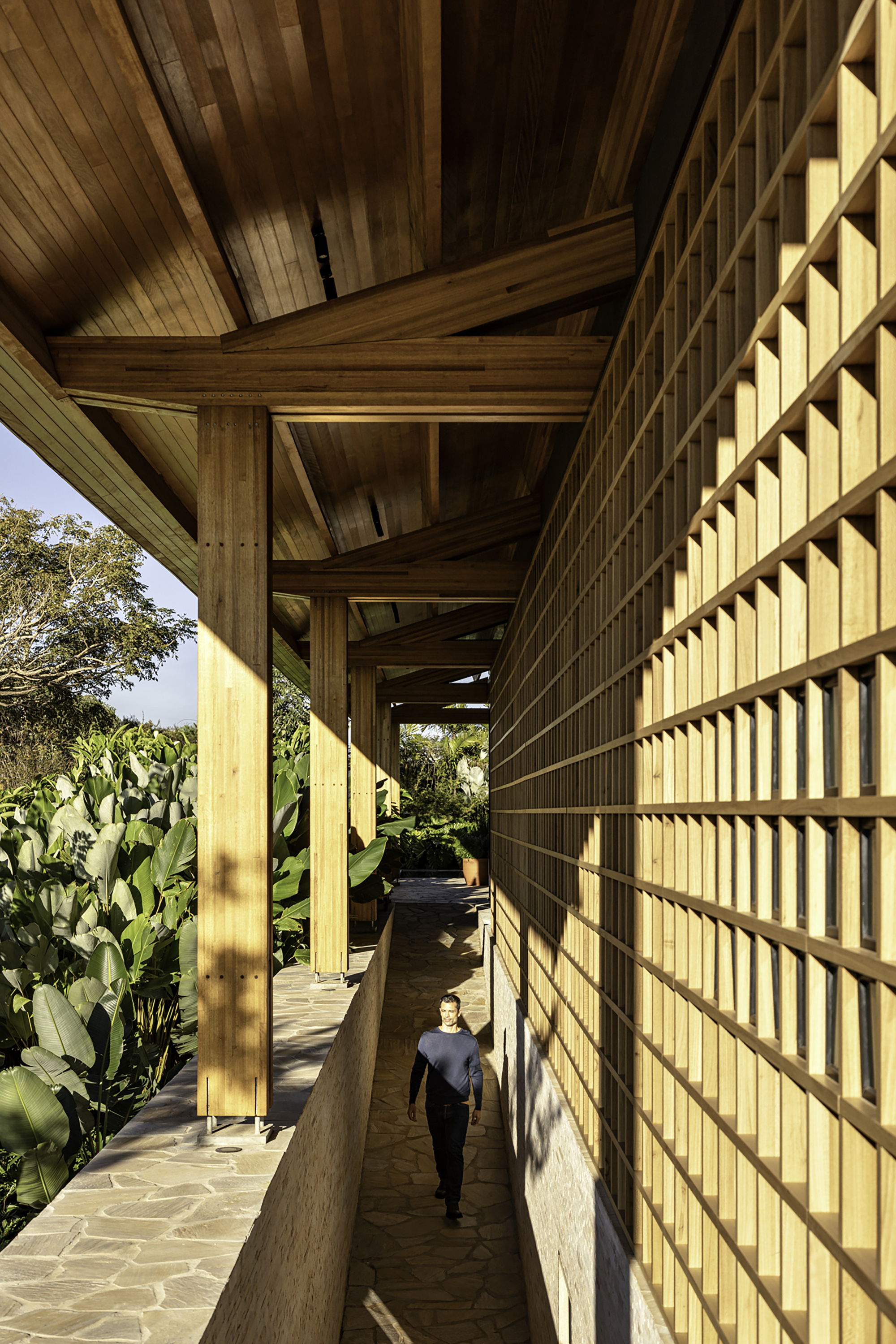 Exterior corridor with timber lattice screen and figure walking in afternoon shadow