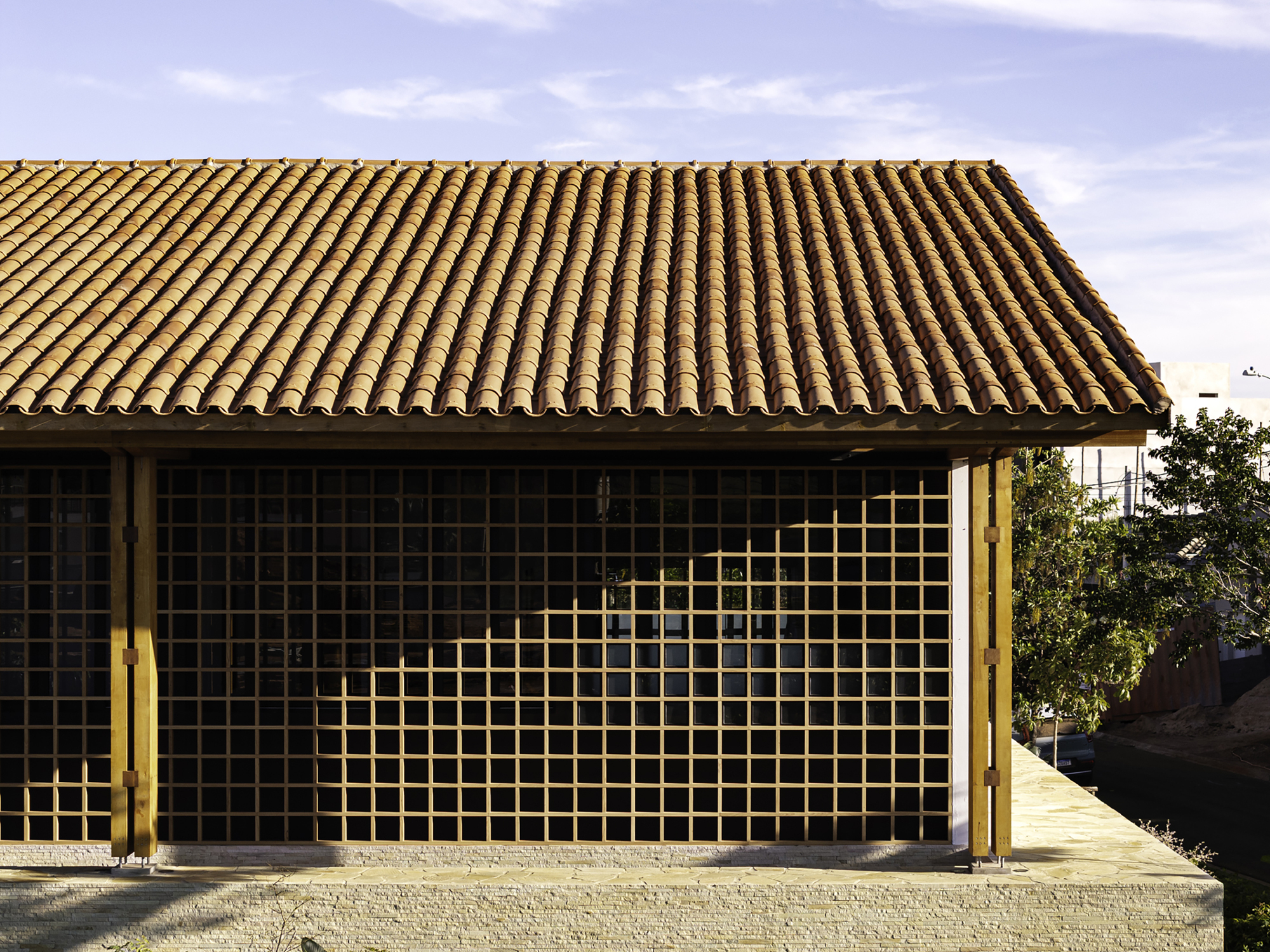 Facade with timber grid screen beneath a clay tile roof under overcast sky