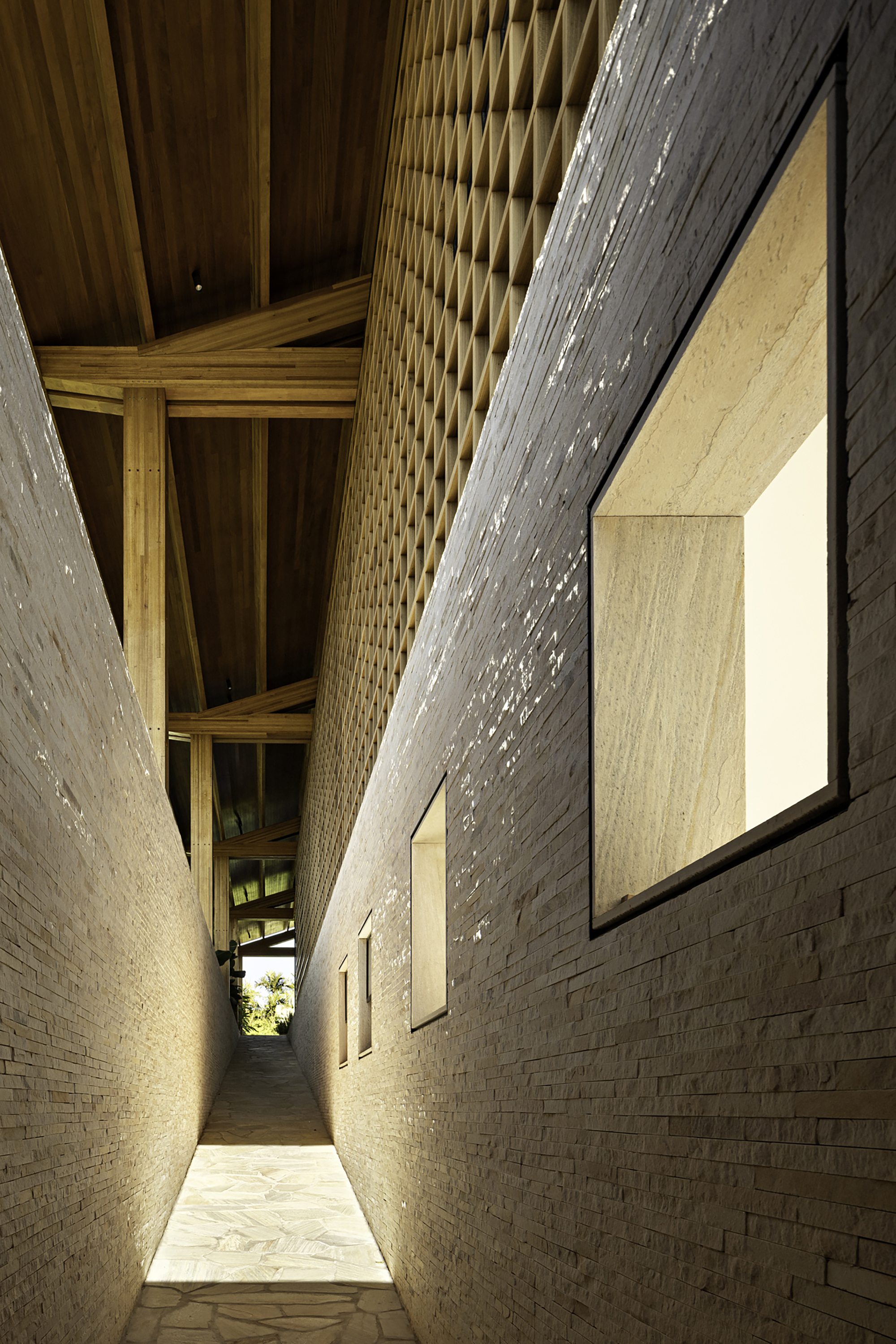 Narrow passage between pale brick walls with exposed timber roof structure at dusk