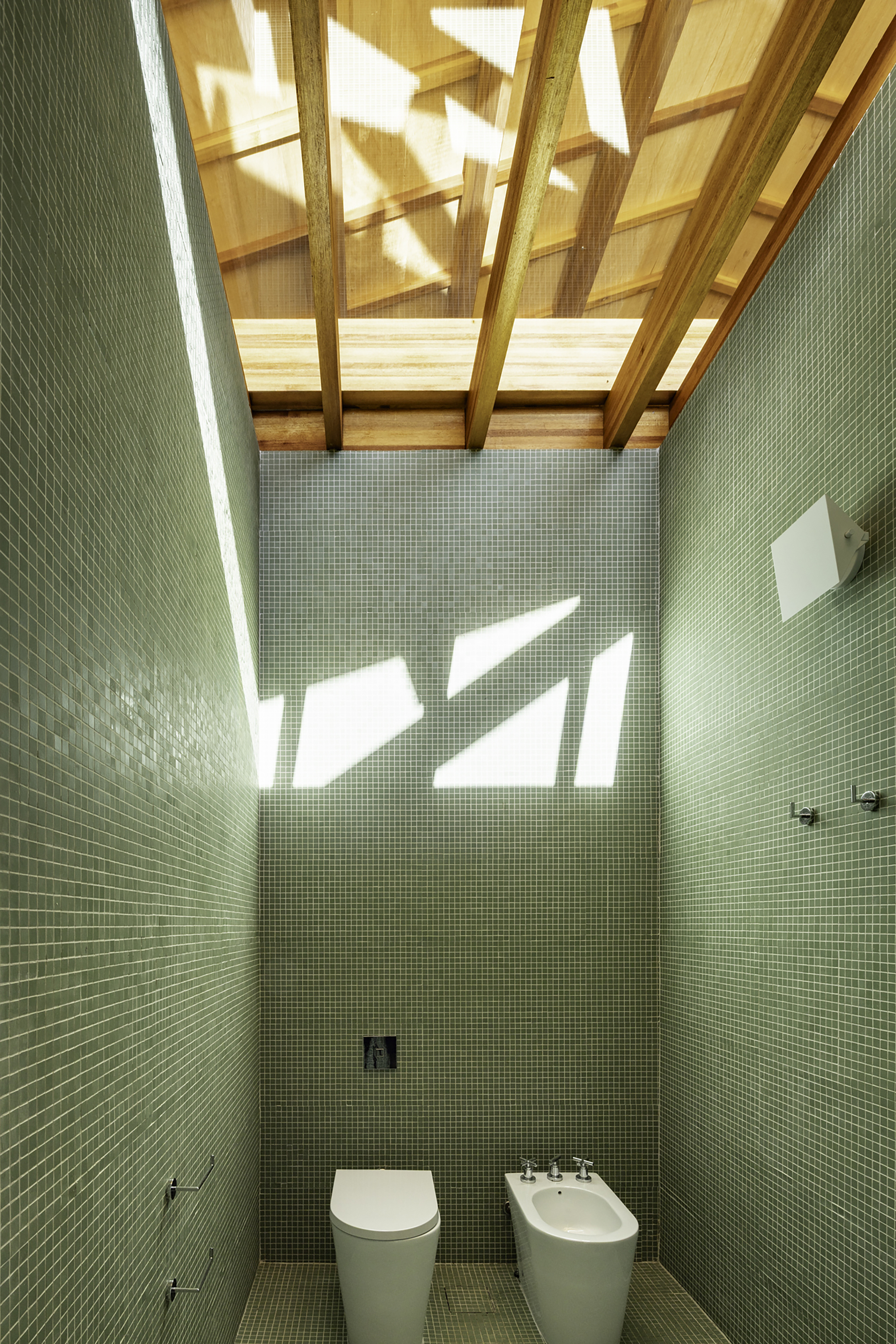 Bathroom clad in green mosaic tile with skylights casting geometric shadows overhead