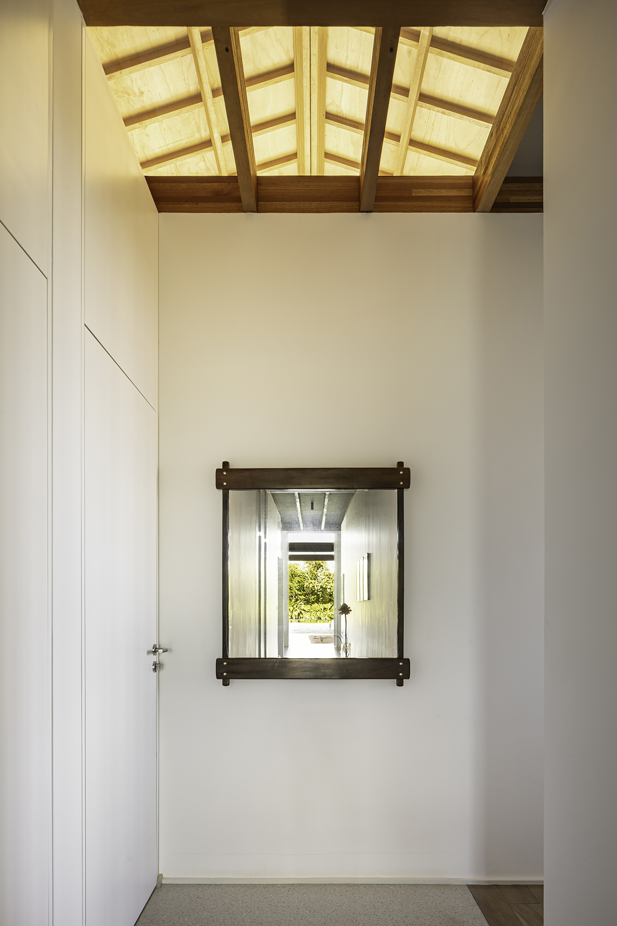 White-walled interior room with timber skylight above and dark-framed window opening framing garden view