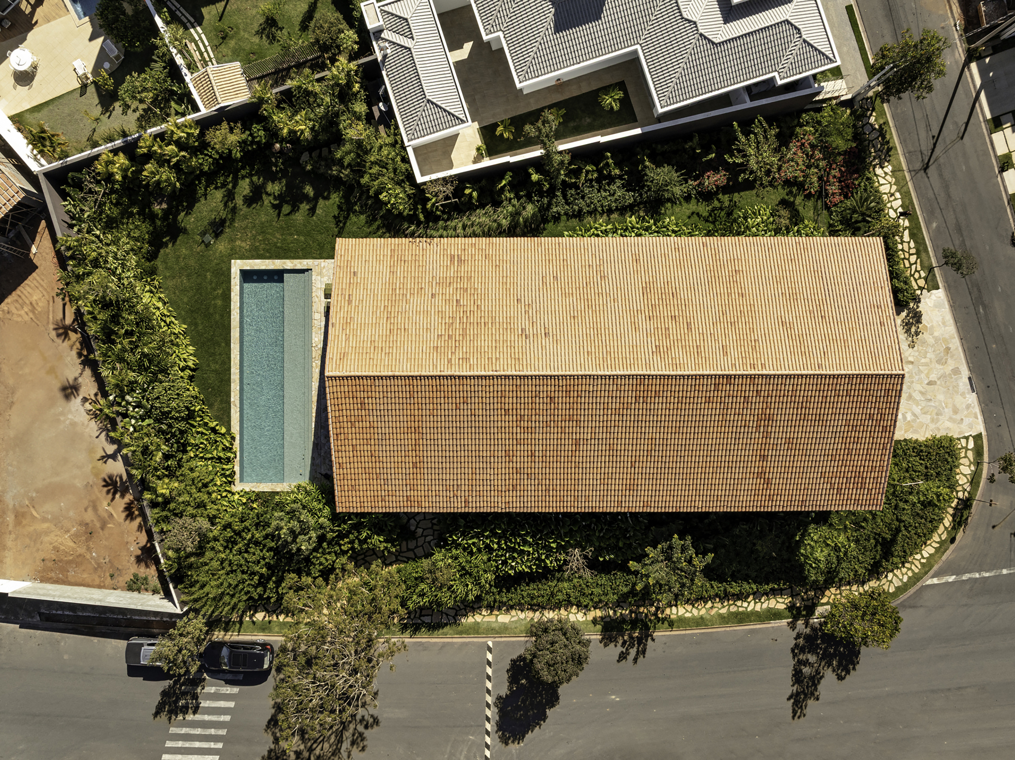 Aerial view of tiled roof volume beside rectangular pool surrounded by mature trees and garden plantings