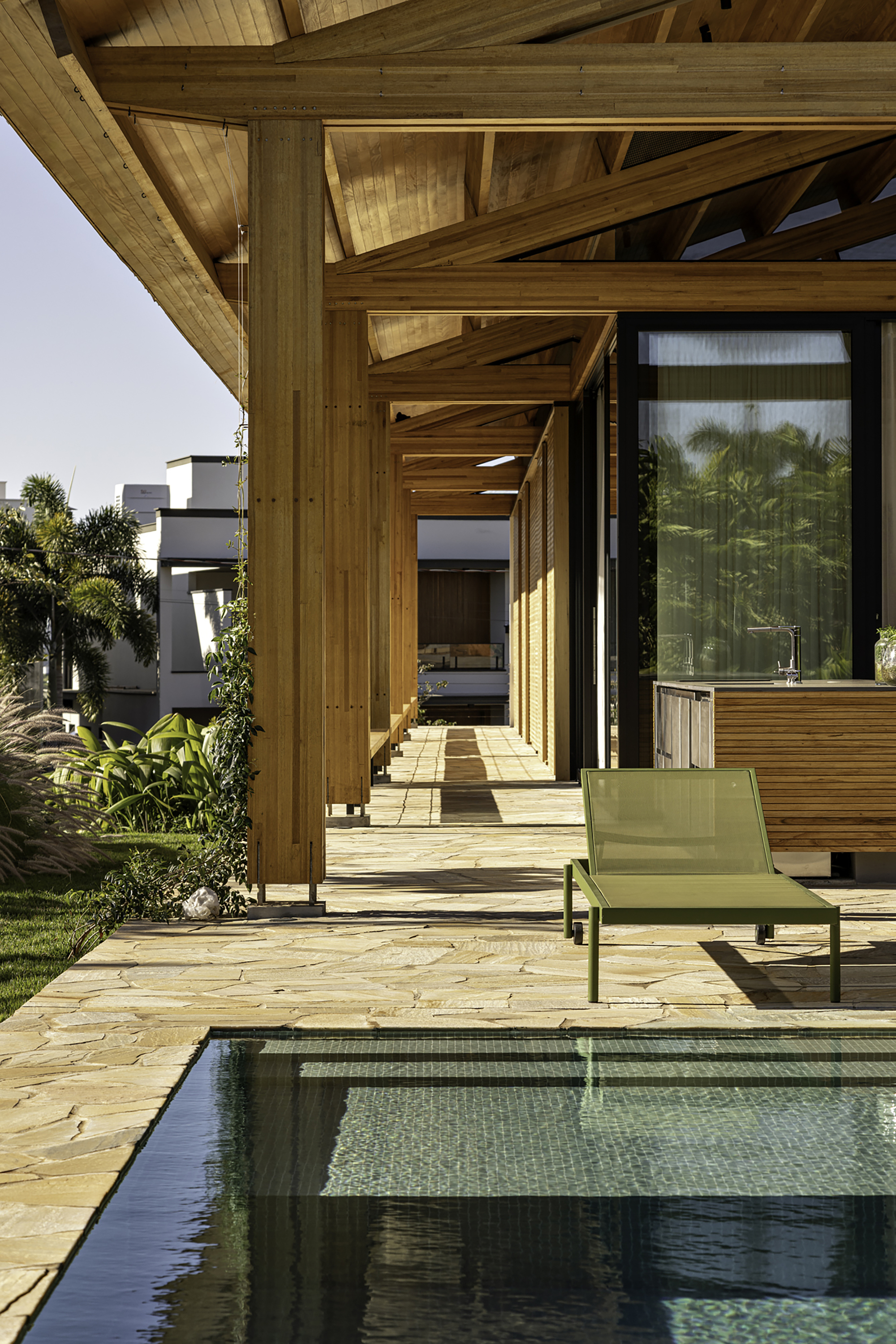 Exterior terrace with small pool, timber structure and green lounge chair overlooking lawn and palms