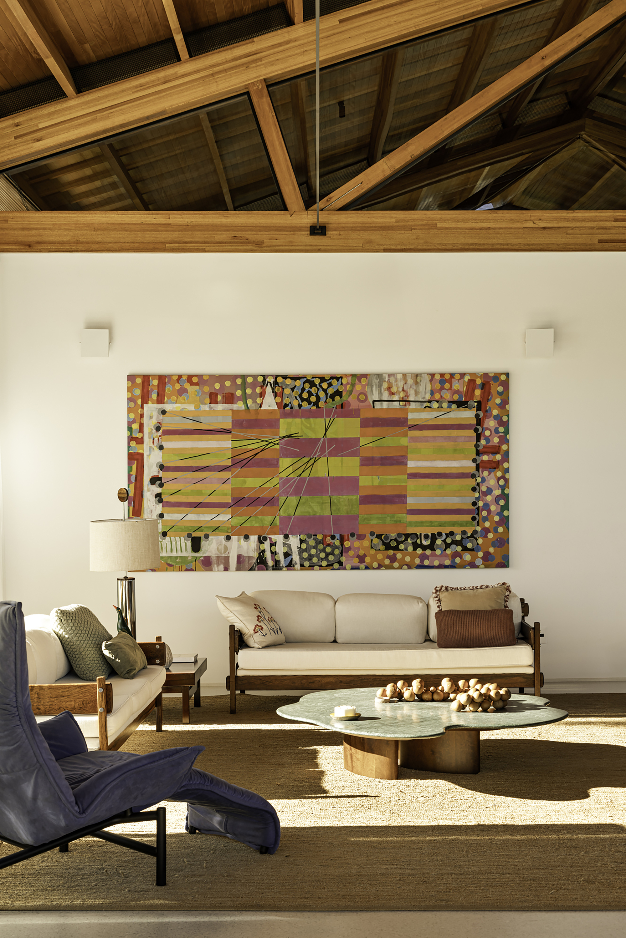 Living room with exposed timber truss ceiling and abstract artwork above a low sofa in afternoon light