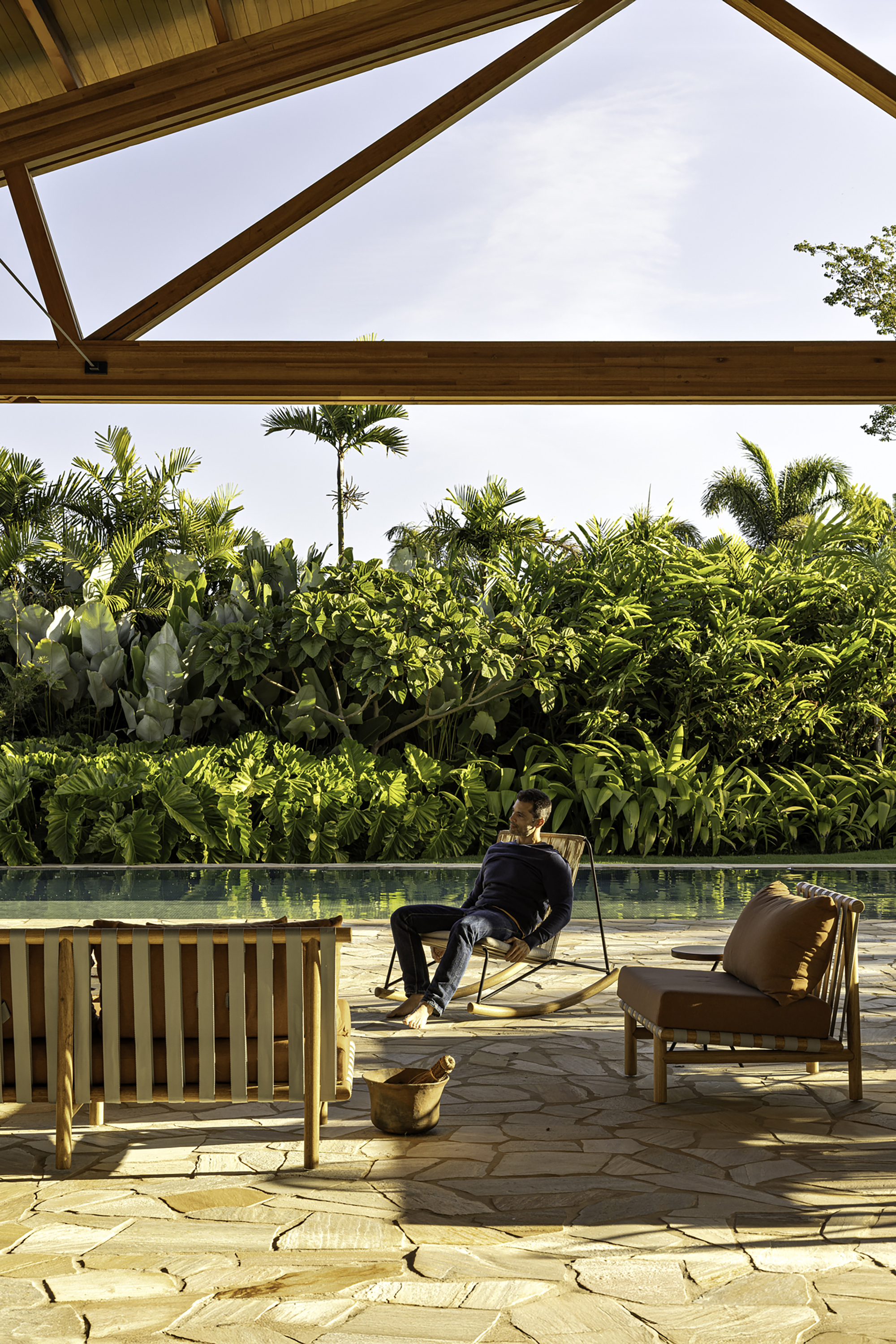 Covered terrace with stone paving and timber benches beside a pool backed by dense tropical planting
