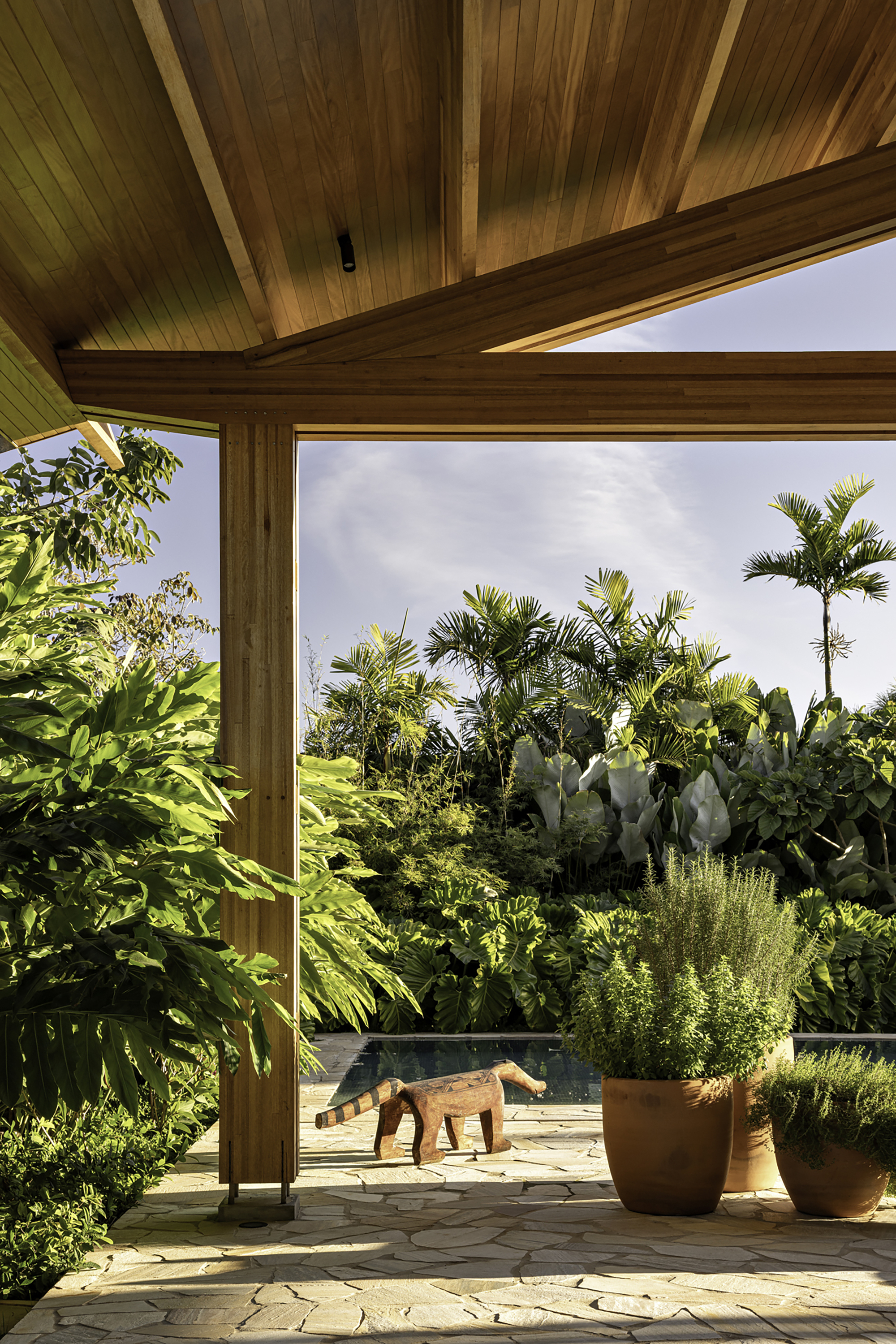 Corner window framing a terrace with planted pots and tropical palms under an overcast sky