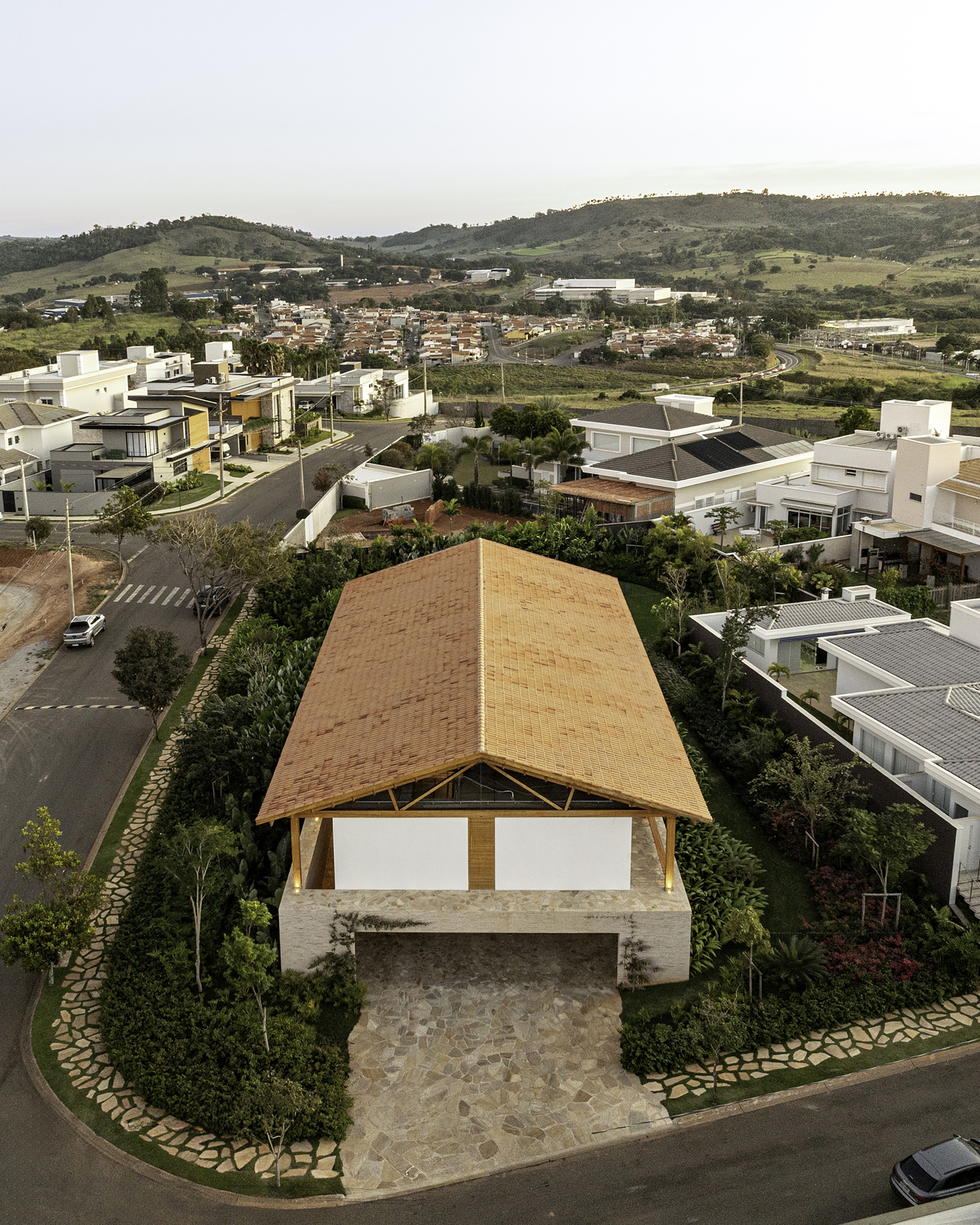 Aerial view of the curved timber roof sheltering a stone terrace within a residential neighborhood