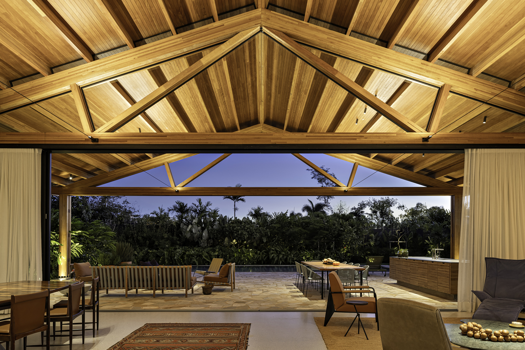 Exposed timber truss ceiling above the open living area looking out to the garden at dusk