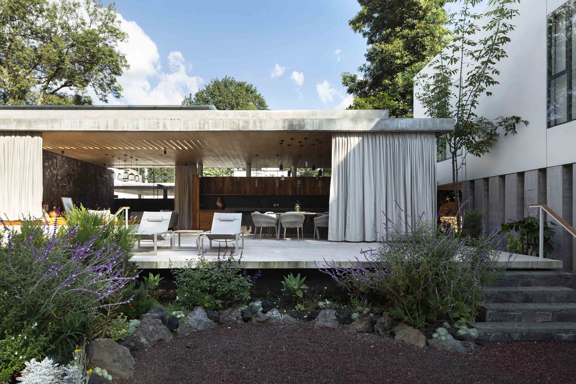 View of the open pavilion across the wild planted garden with curtains drawn back