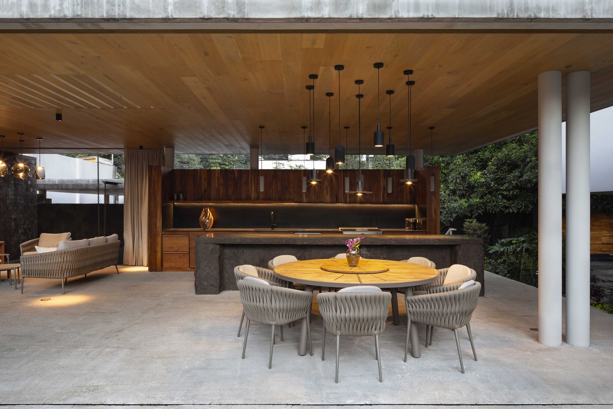 Open dining and kitchen pavilion with a round table, pendant lights and a timber ceiling