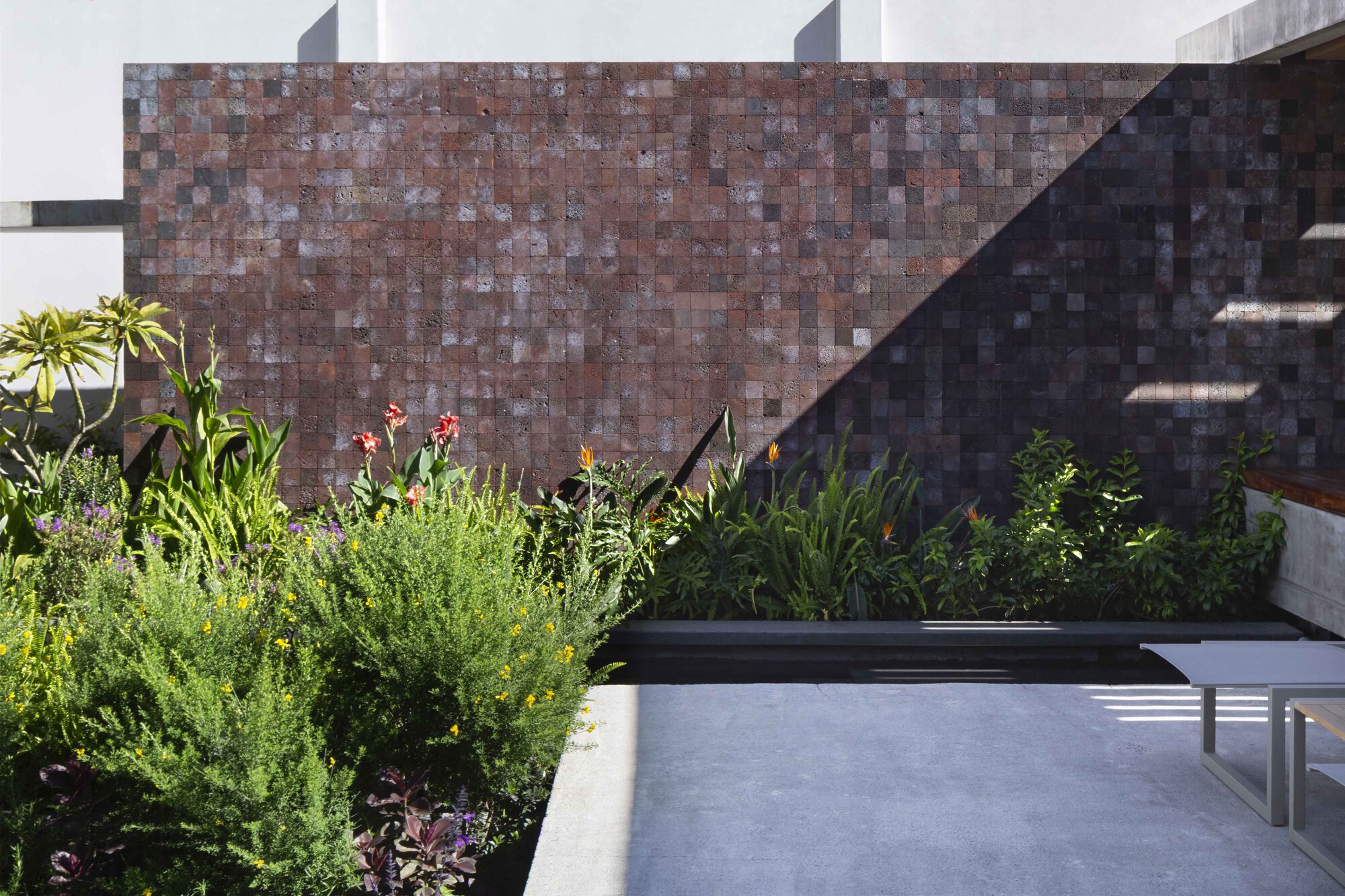 Red volcanic stone tile wall behind a planted bed with bird-of-paradise and grasses