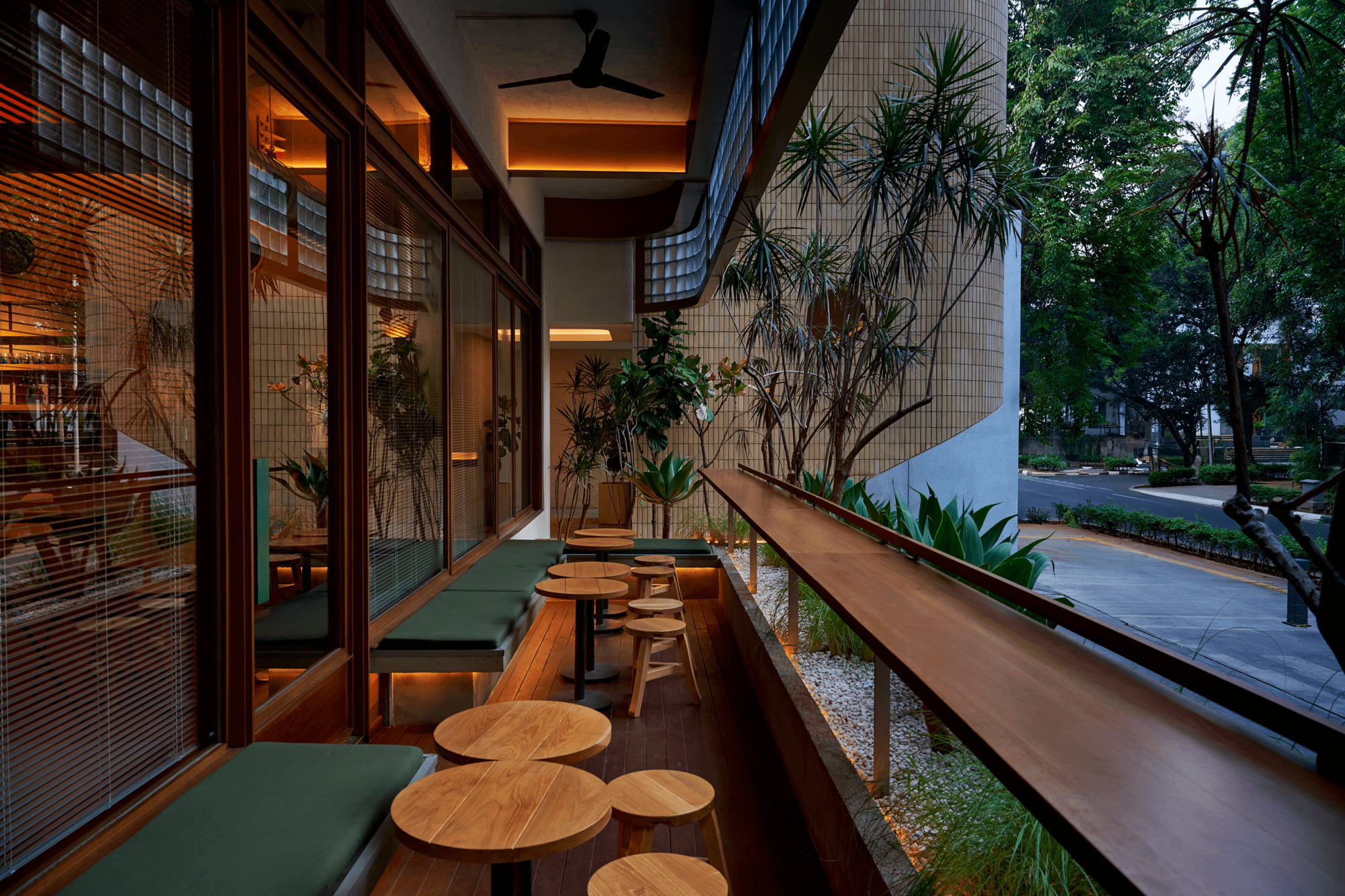 Covered balcony seating area with timber benches and stools under exposed ceiling beams at dusk
