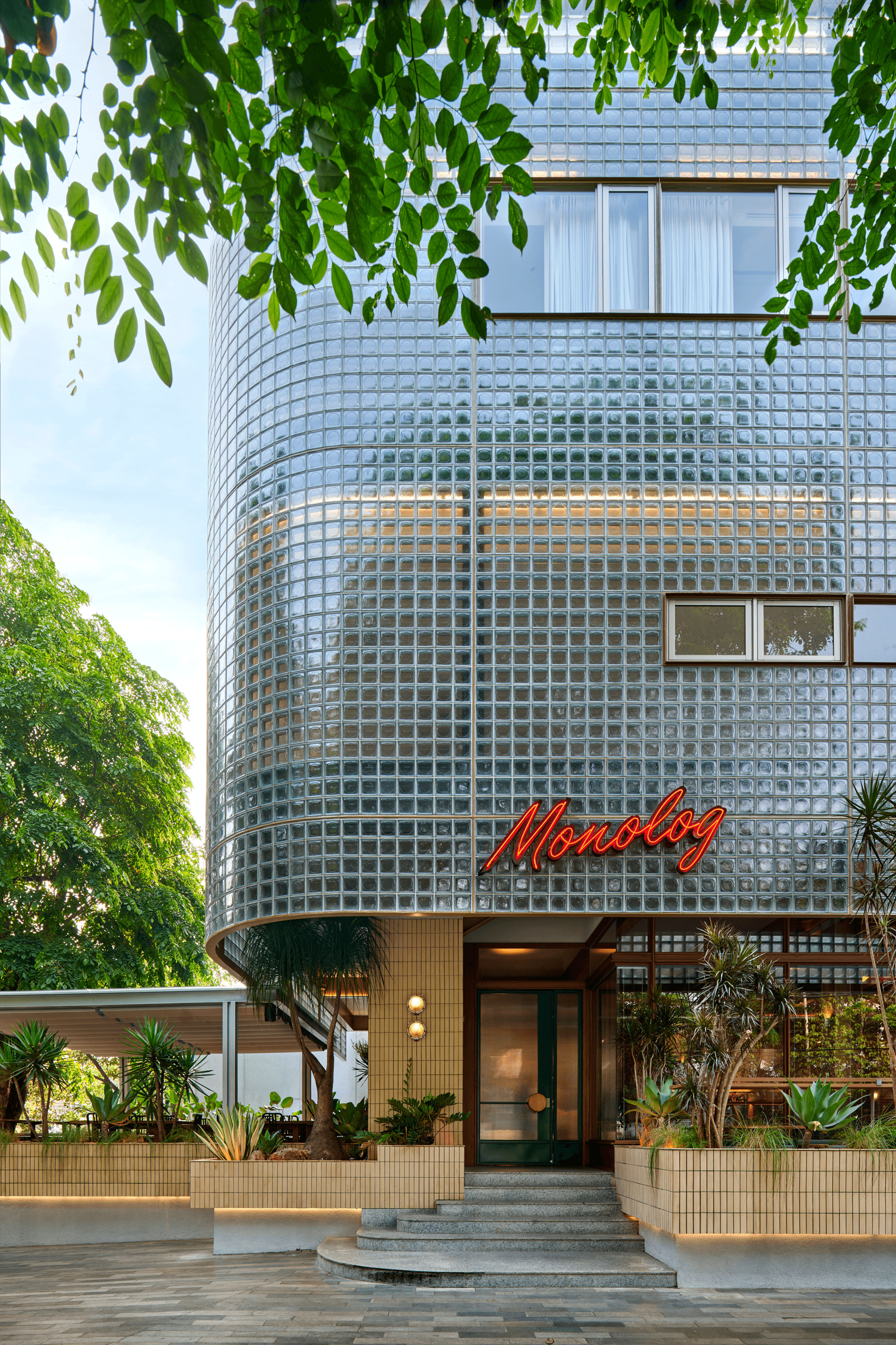 Entry facade with curved glass block wall above planted beds visible through overhanging tree branches