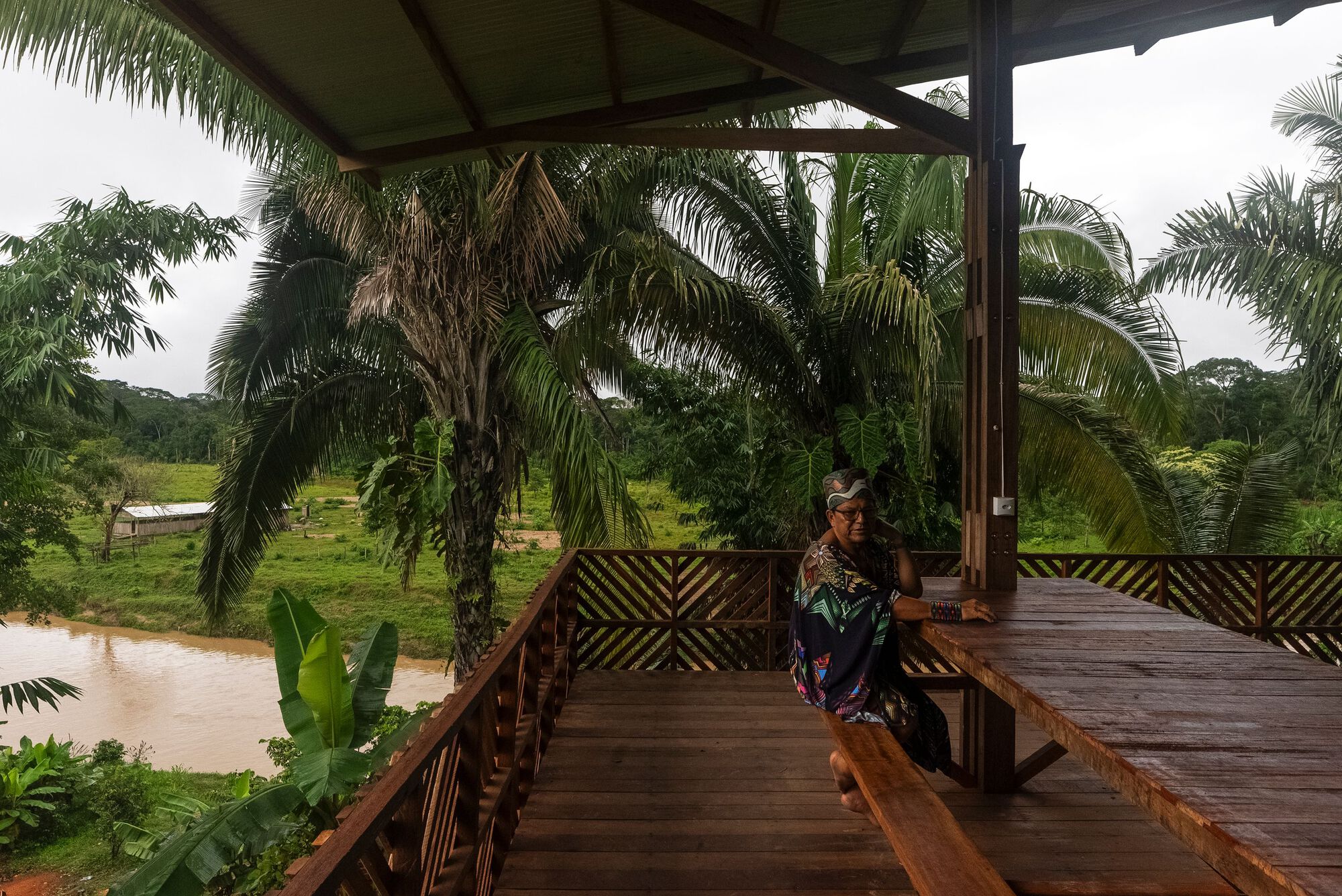 Covered timber deck with patterned railing overlooking palm trees and river during overcast weather