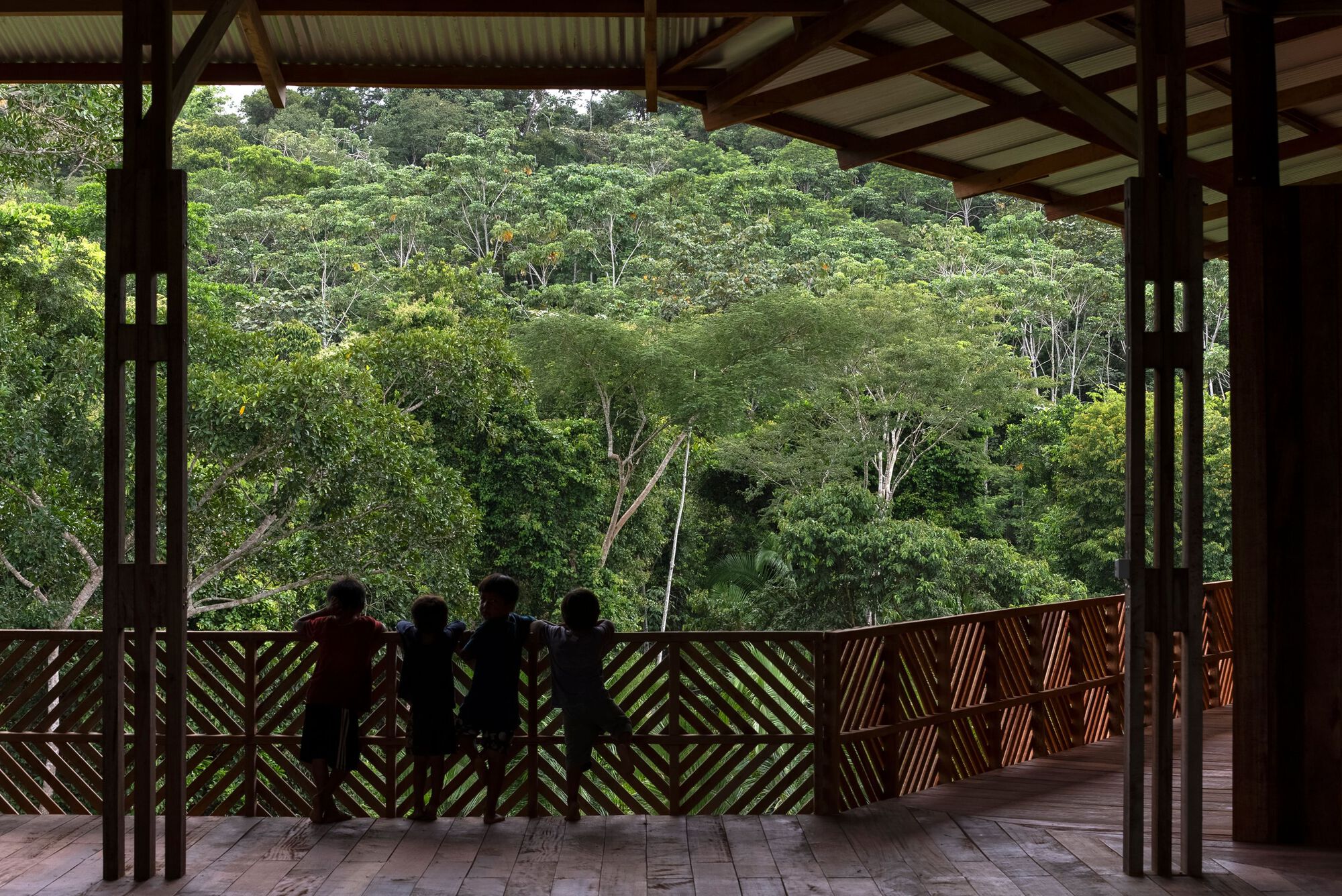 Four silhouetted figures standing at geometric timber balustrade framing dense tropical forest hillside