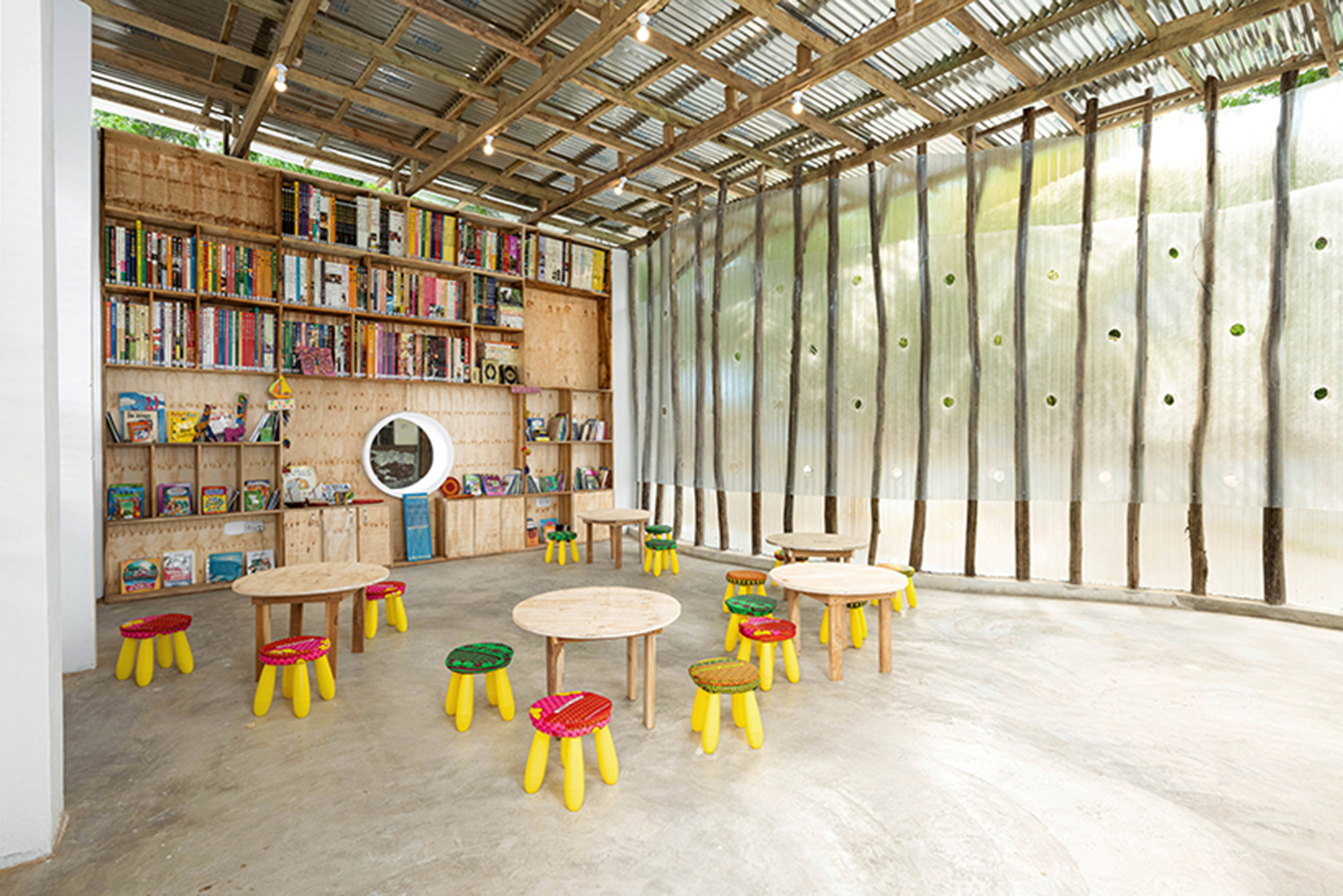 Library interior with plywood shelving along one wall and low tables on polished concrete floor