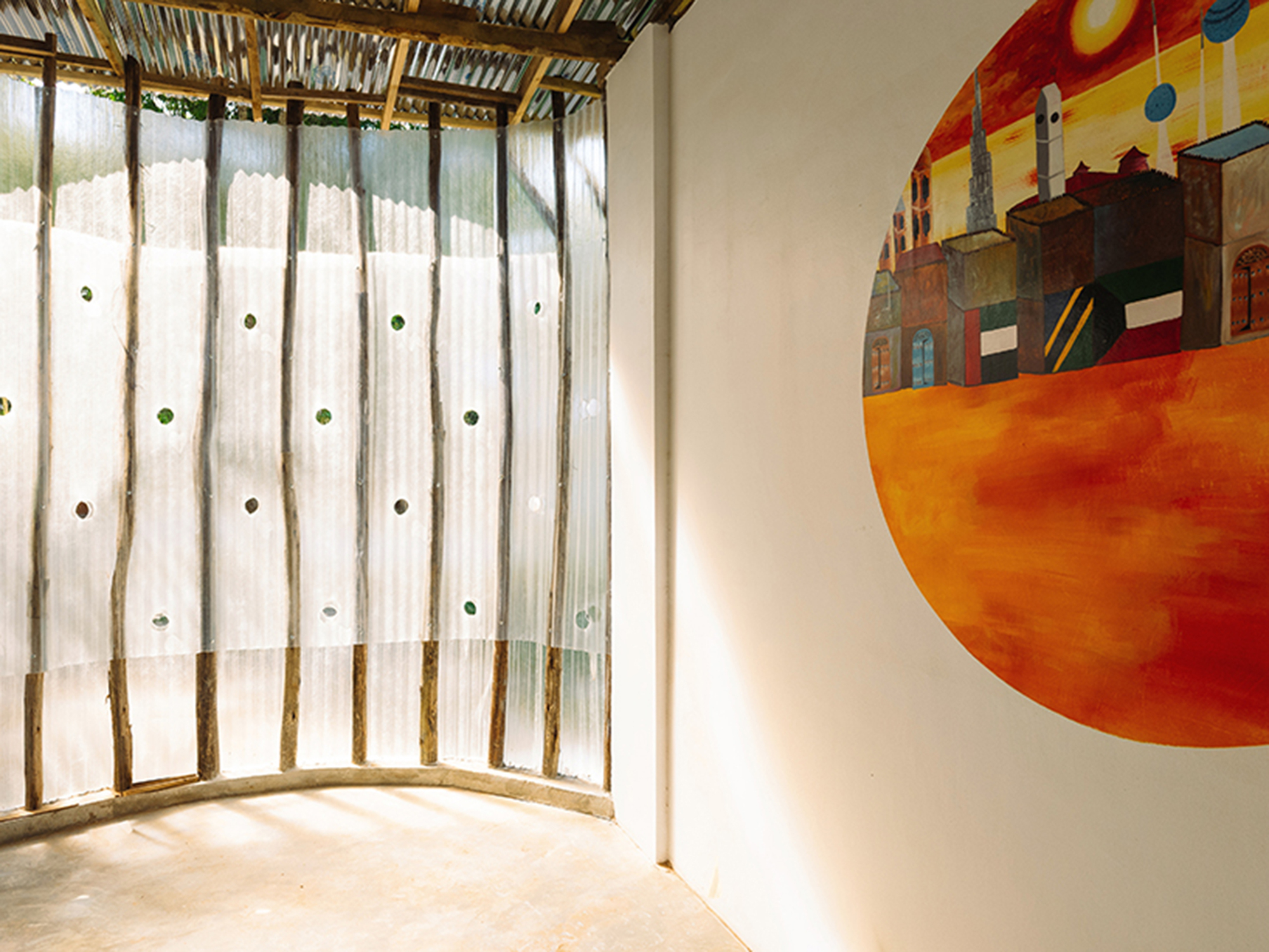Detail of curved translucent wall with circular glass openings and a painted mural on adjacent surface