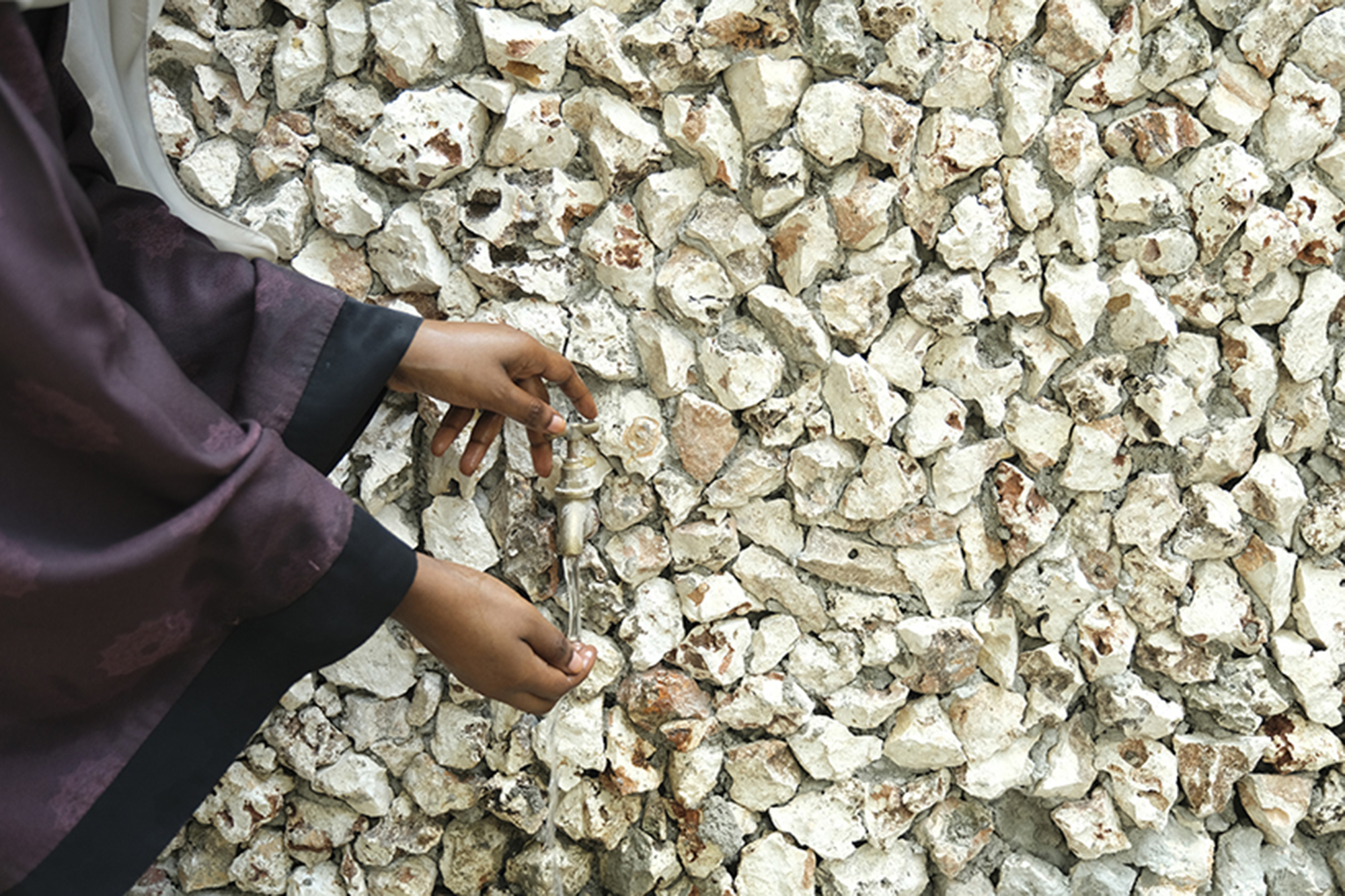 Hands touching a wall surface composed of white crushed coral or oyster shell aggregate