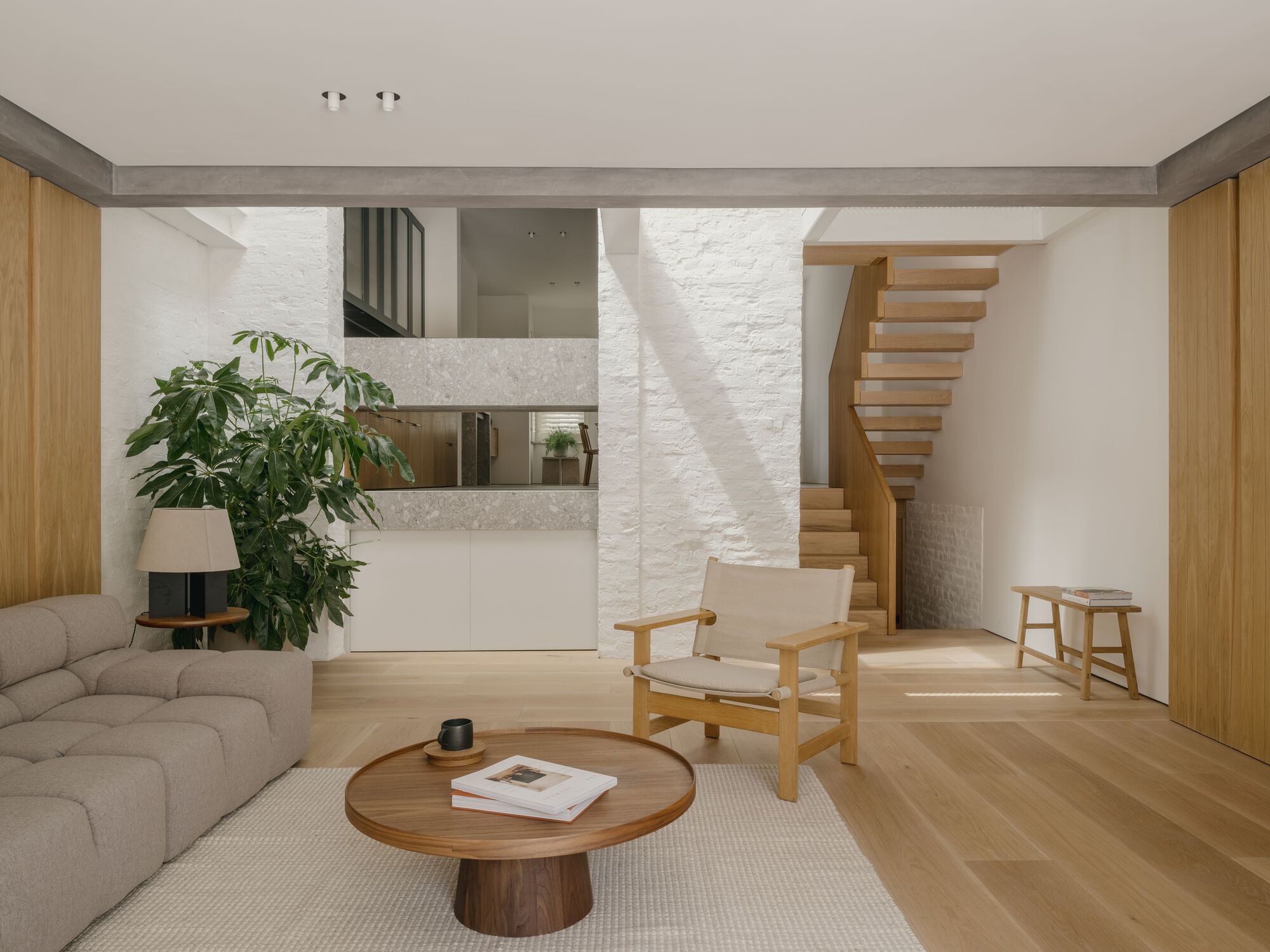 Double-height living space with curved timber staircase and white brick wall under natural daylight