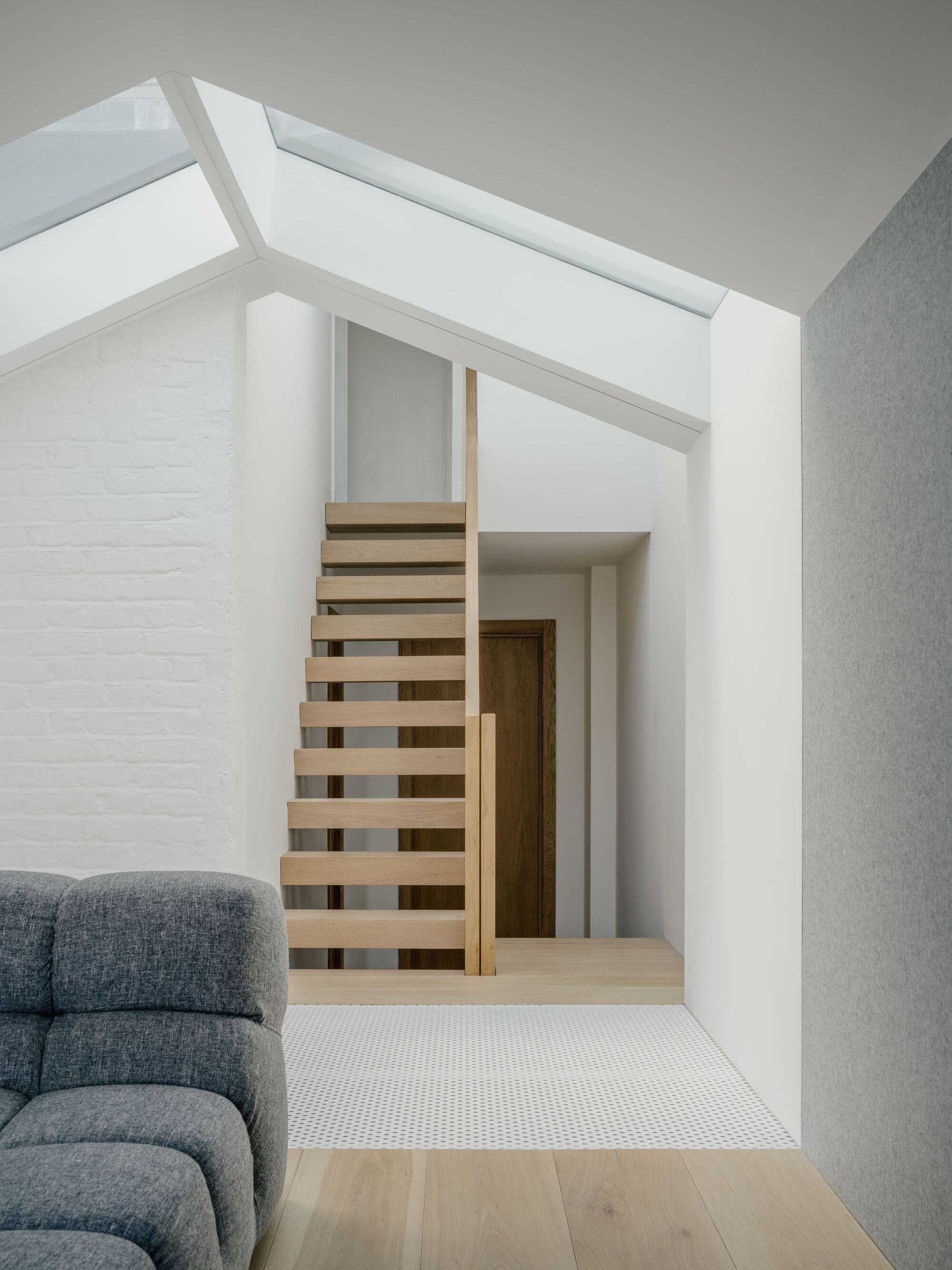 Open-tread timber staircase beneath a linear skylight beside painted white brick wall