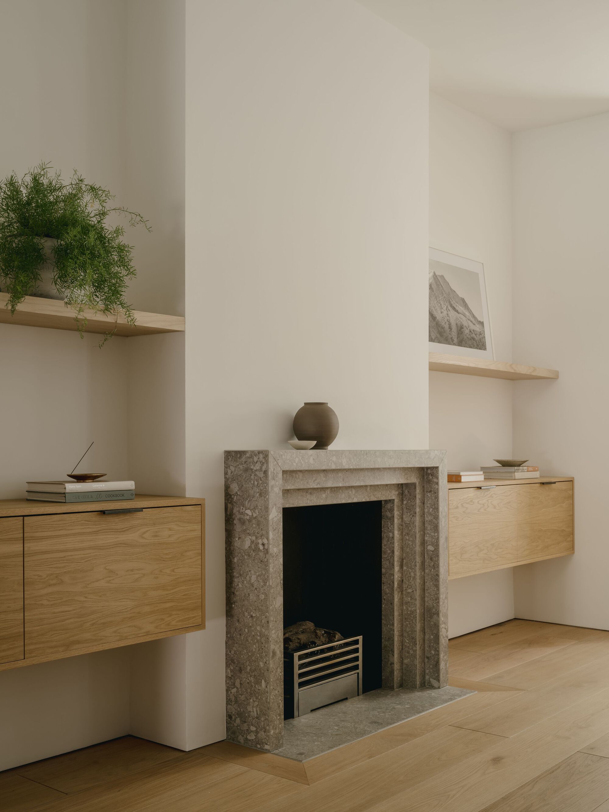 Grey stone fireplace surround flanked by suspended oak cabinetry and floating timber shelves