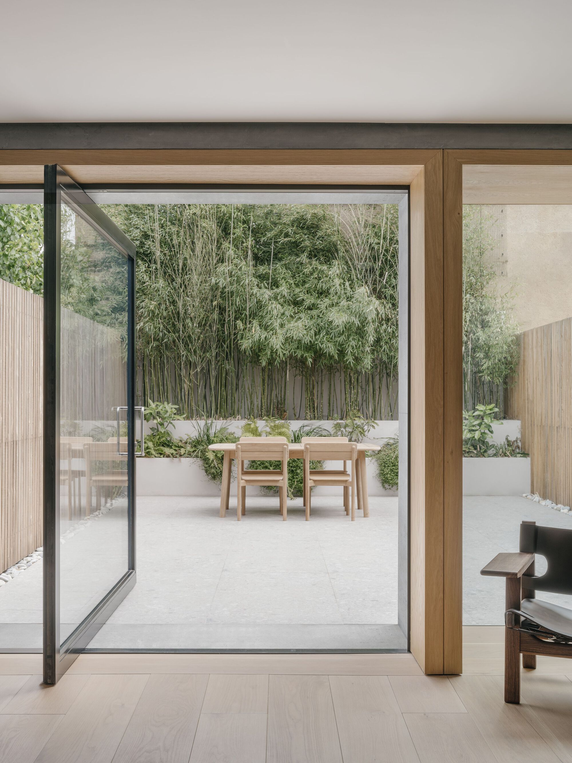 Pivoting steel-framed glass door opening onto a paved courtyard with bamboo and planted beds