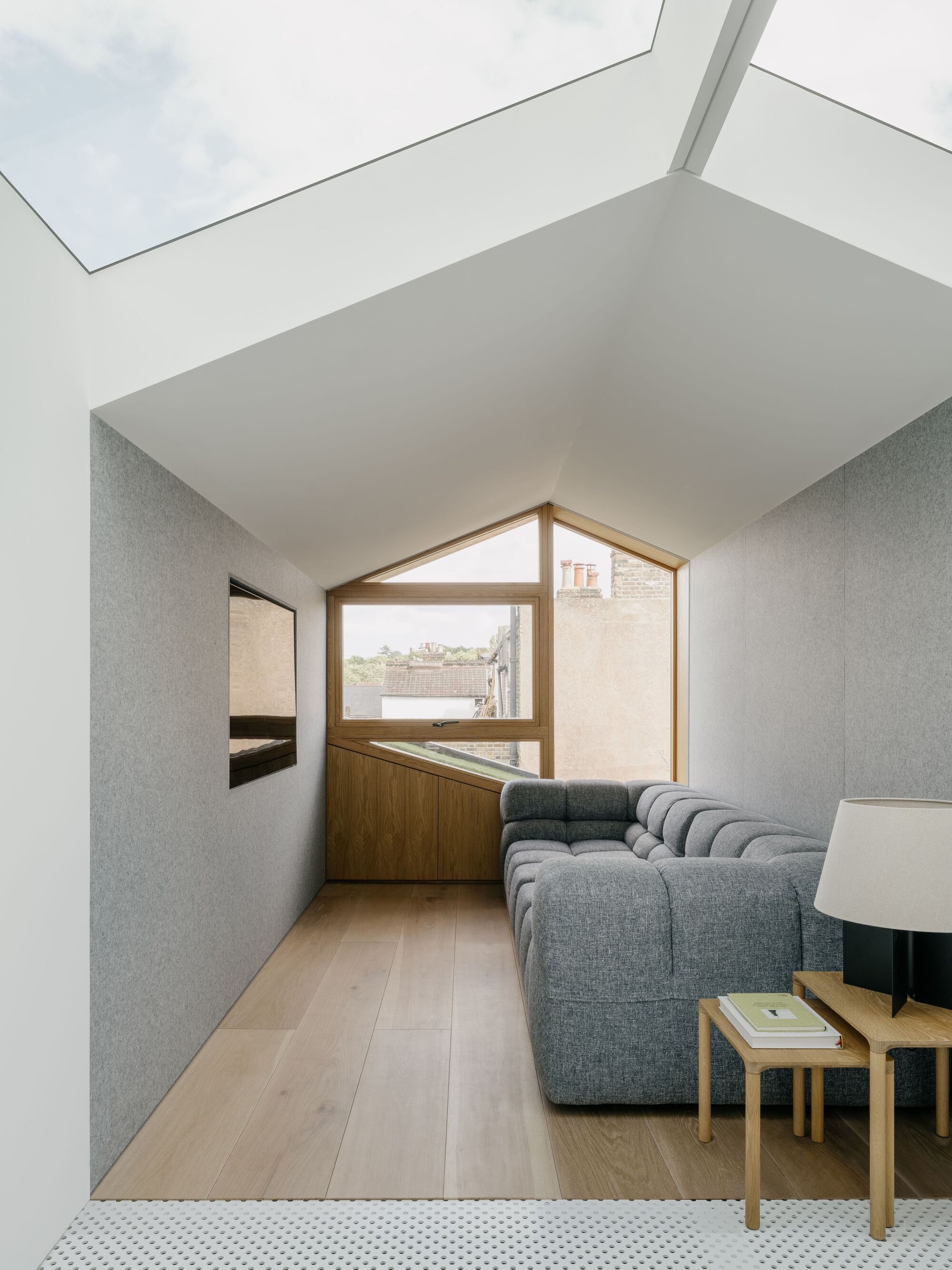 Gabled window framing rooftops beyond a living room with grey sofa and skylight above