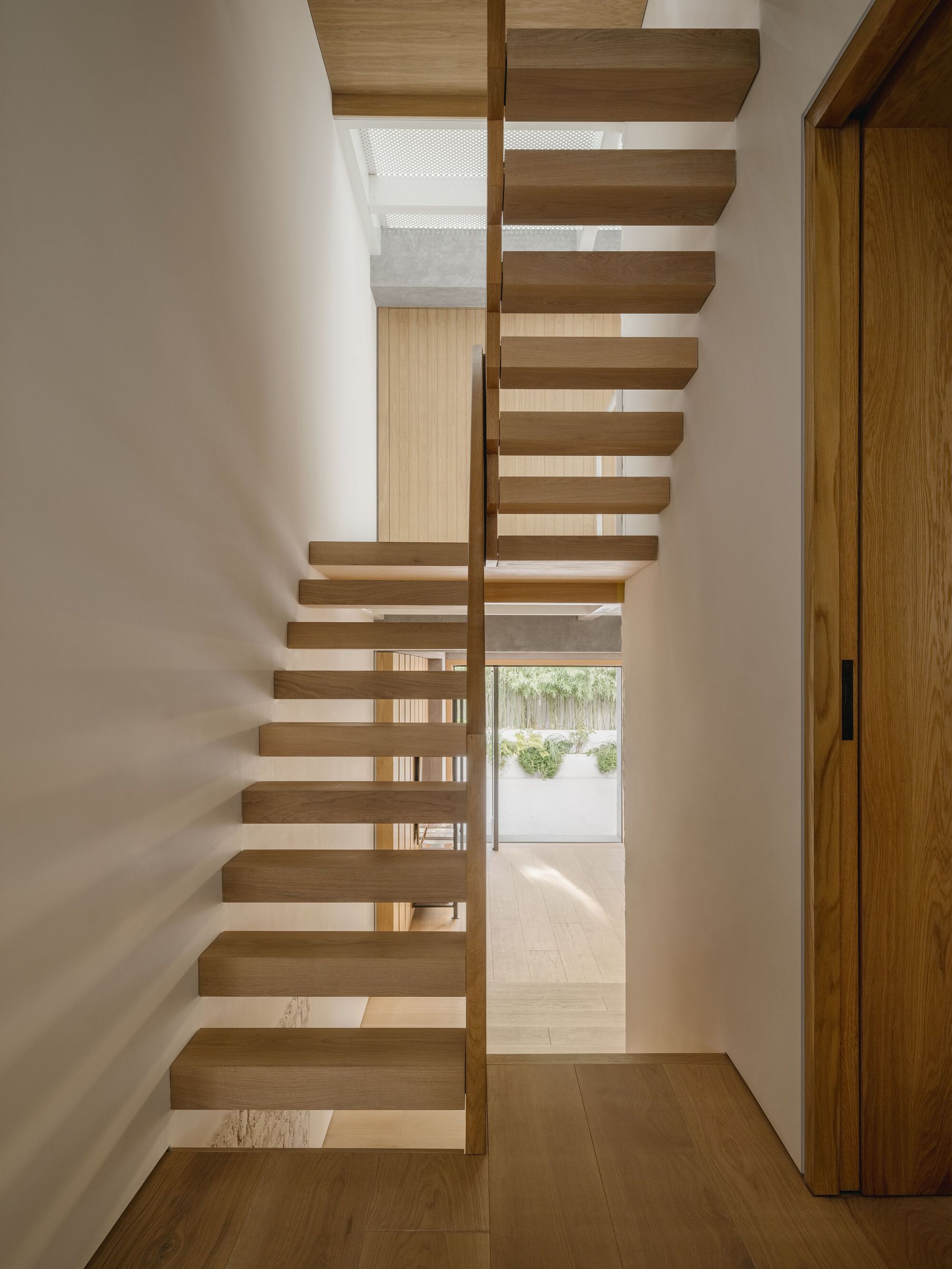 Cantilevered timber staircase with open risers leading to a skylit landing