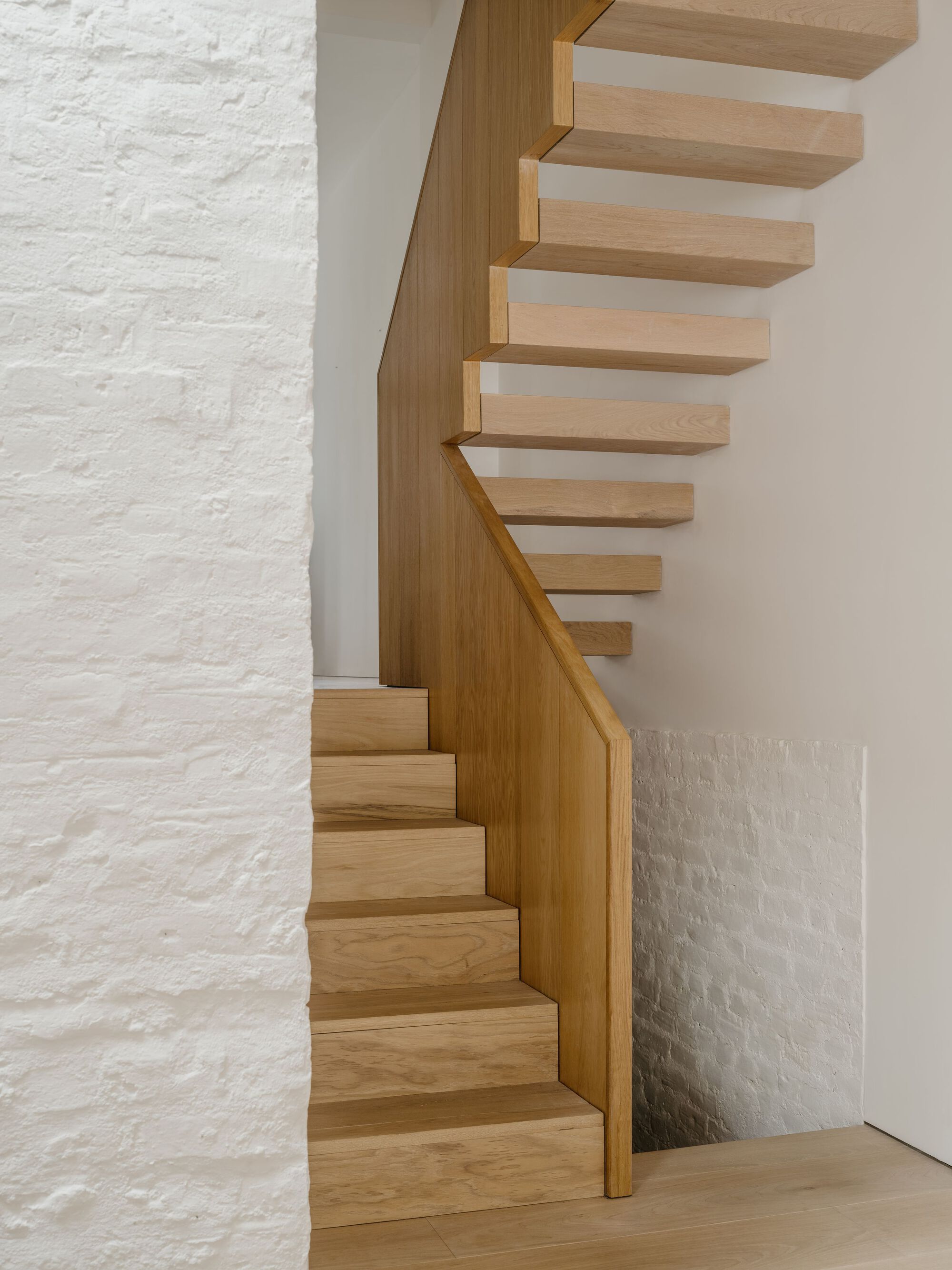 Close-up of the timber staircase turning against a white painted brick wall