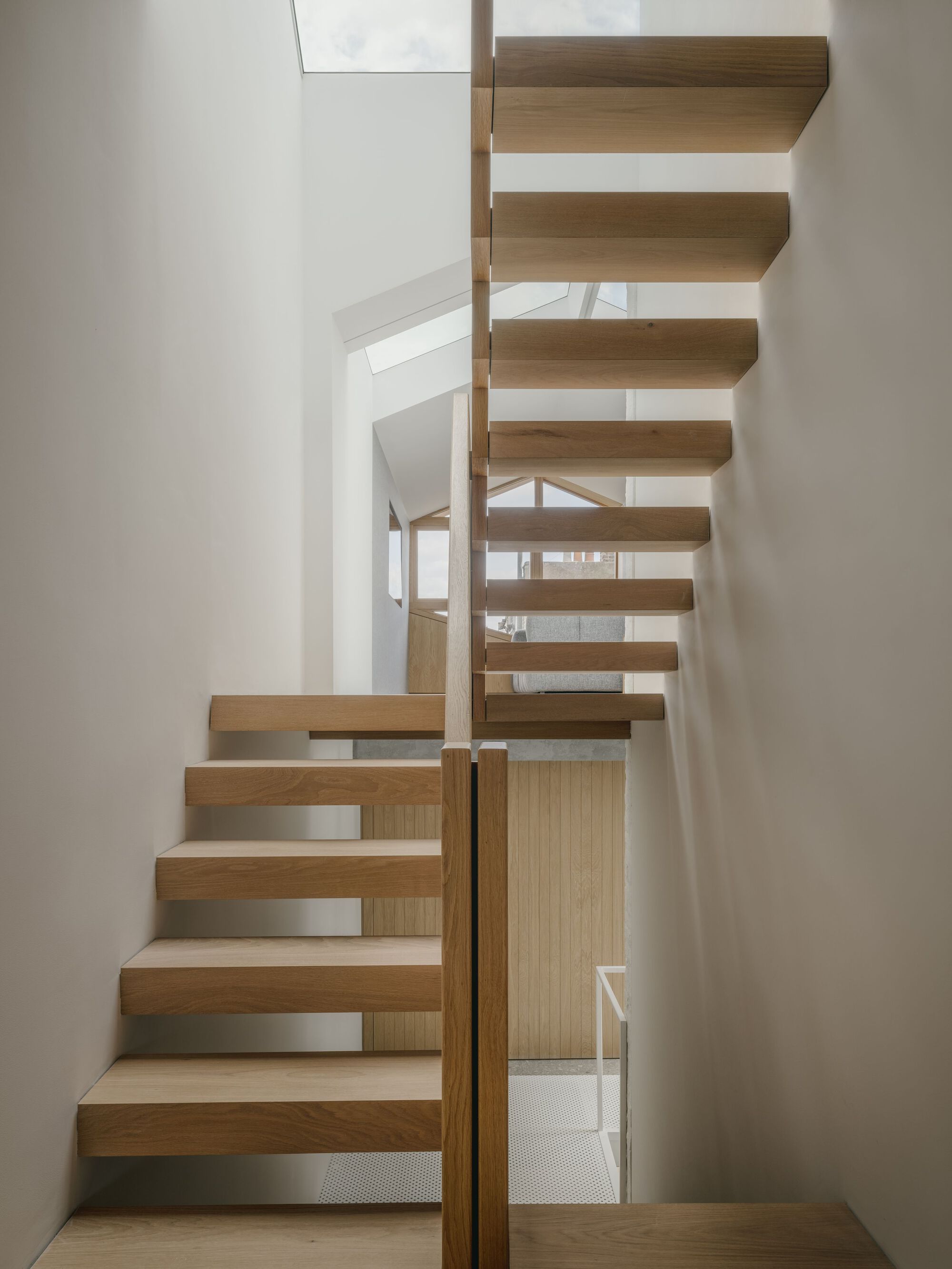 Timber staircase with cantilevered treads and vertical slat balustrade in a white-walled interior