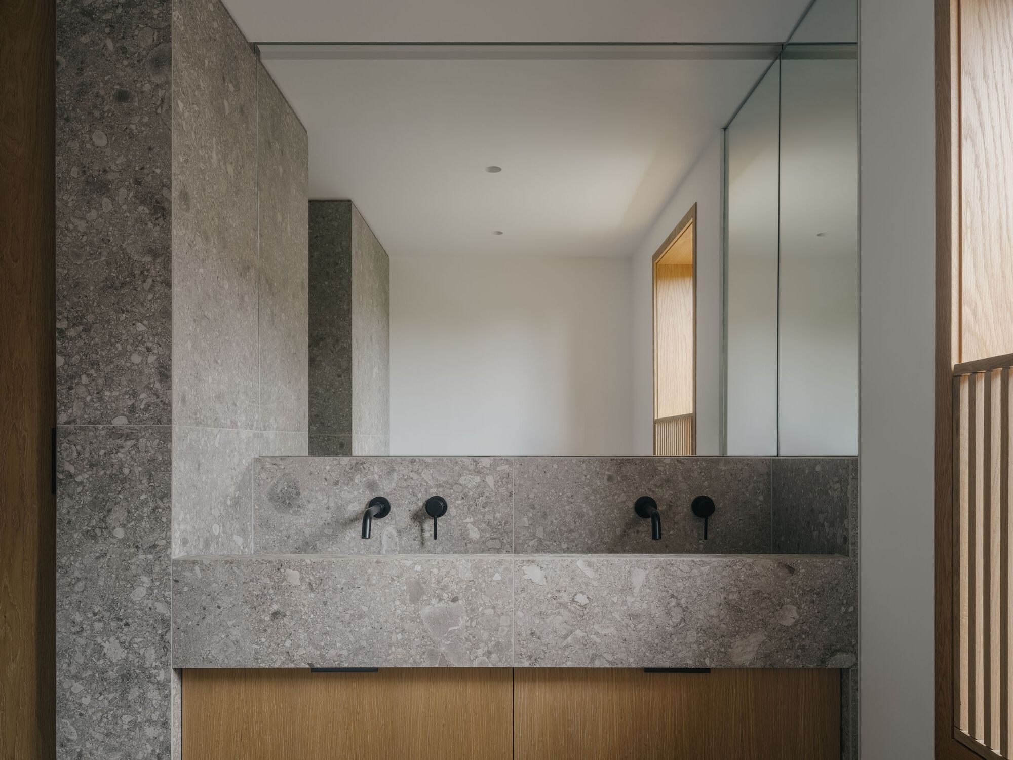 Double vanity with grey limestone and timber cabinetry beneath a full-width mirror in a bathroom