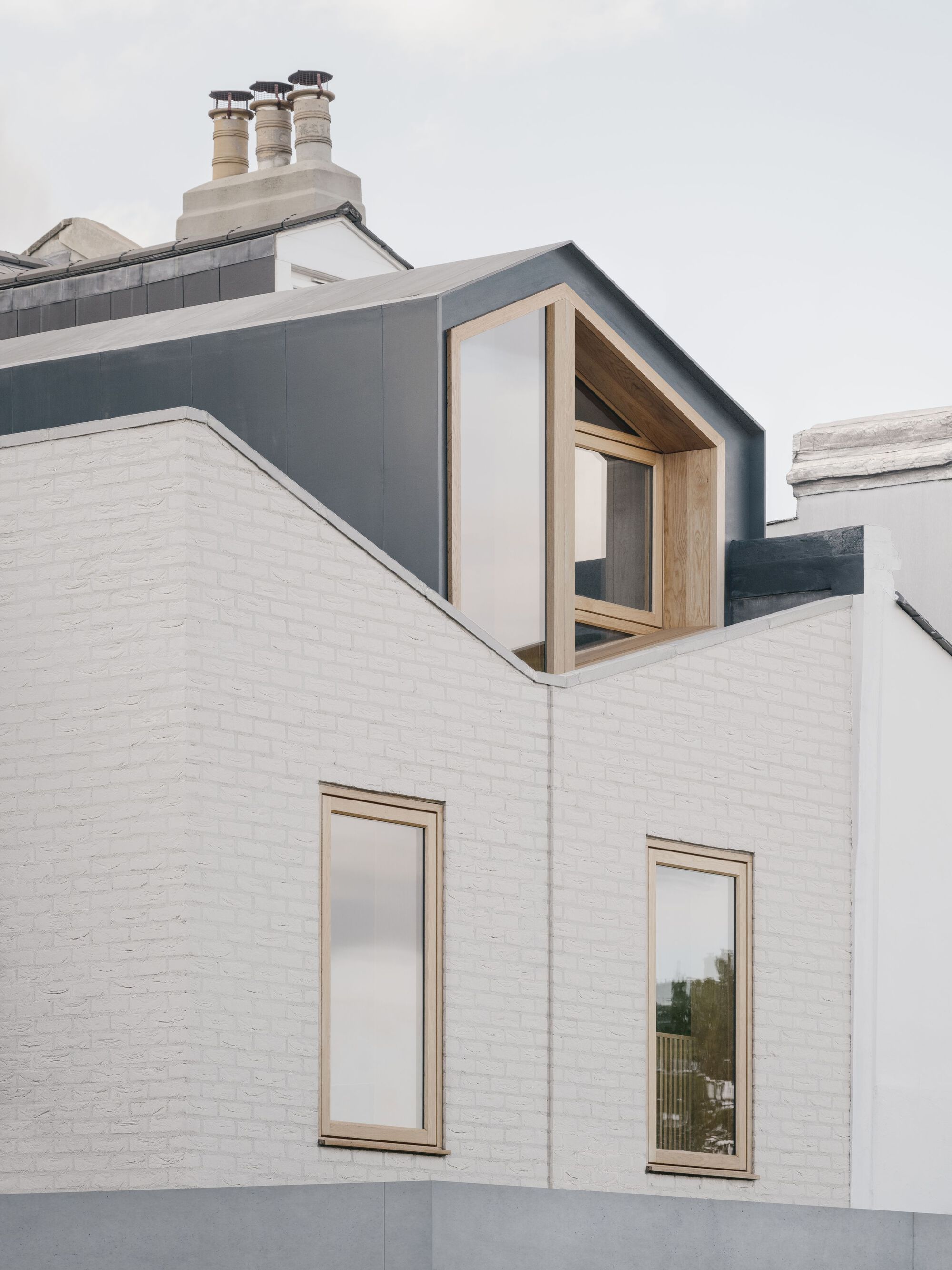Timber-framed dormer window projecting from dark grey zinc roof above white painted brick facade