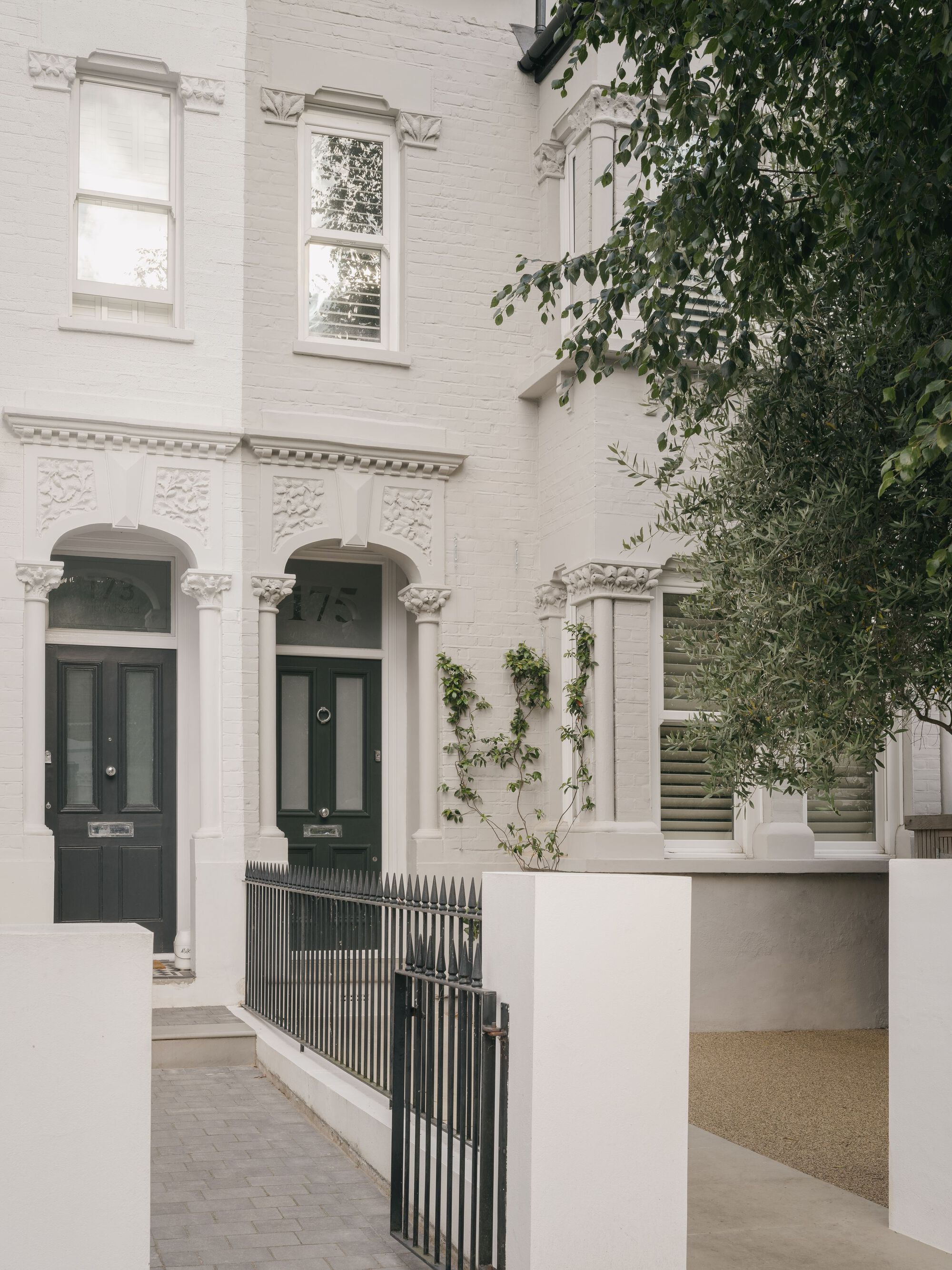 White painted brick facade with arched doorways and climbing vines beside metal railings and gravel path