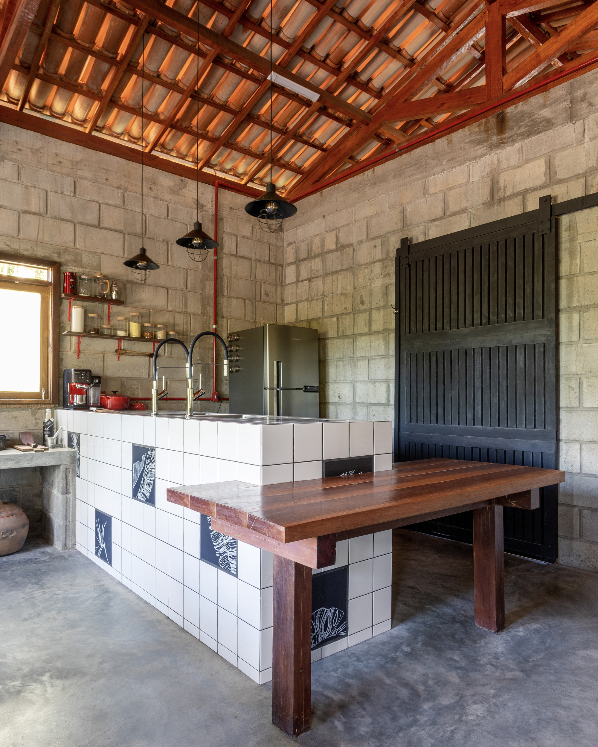 Kitchen island with white tile base, timber countertop and exposed clay tile roof above concrete walls
