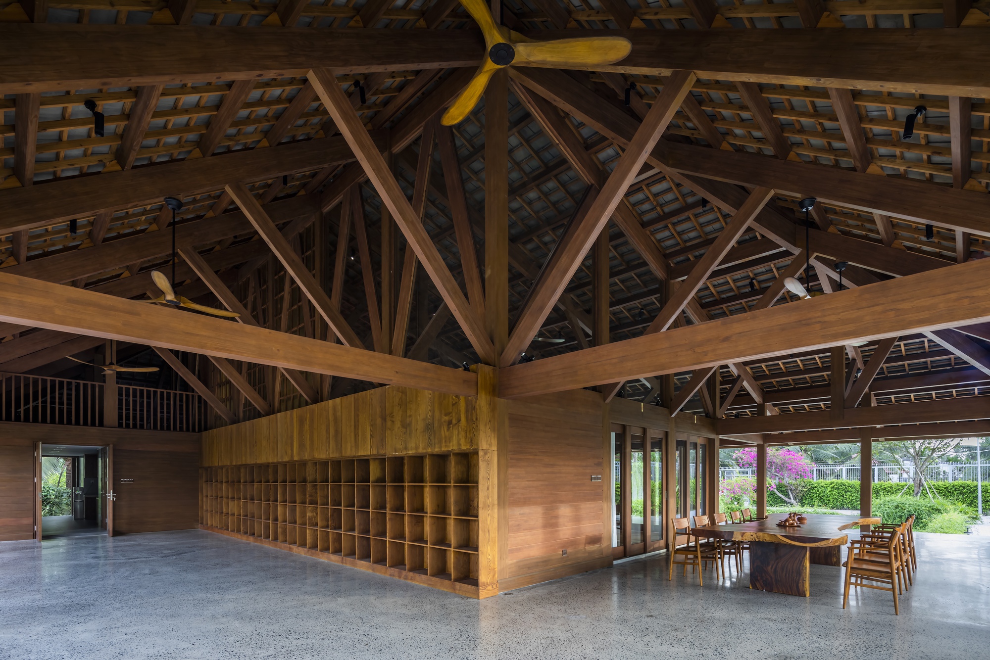 Interior view of exposed timber truss roof structure above a wooden storage unit and dining table