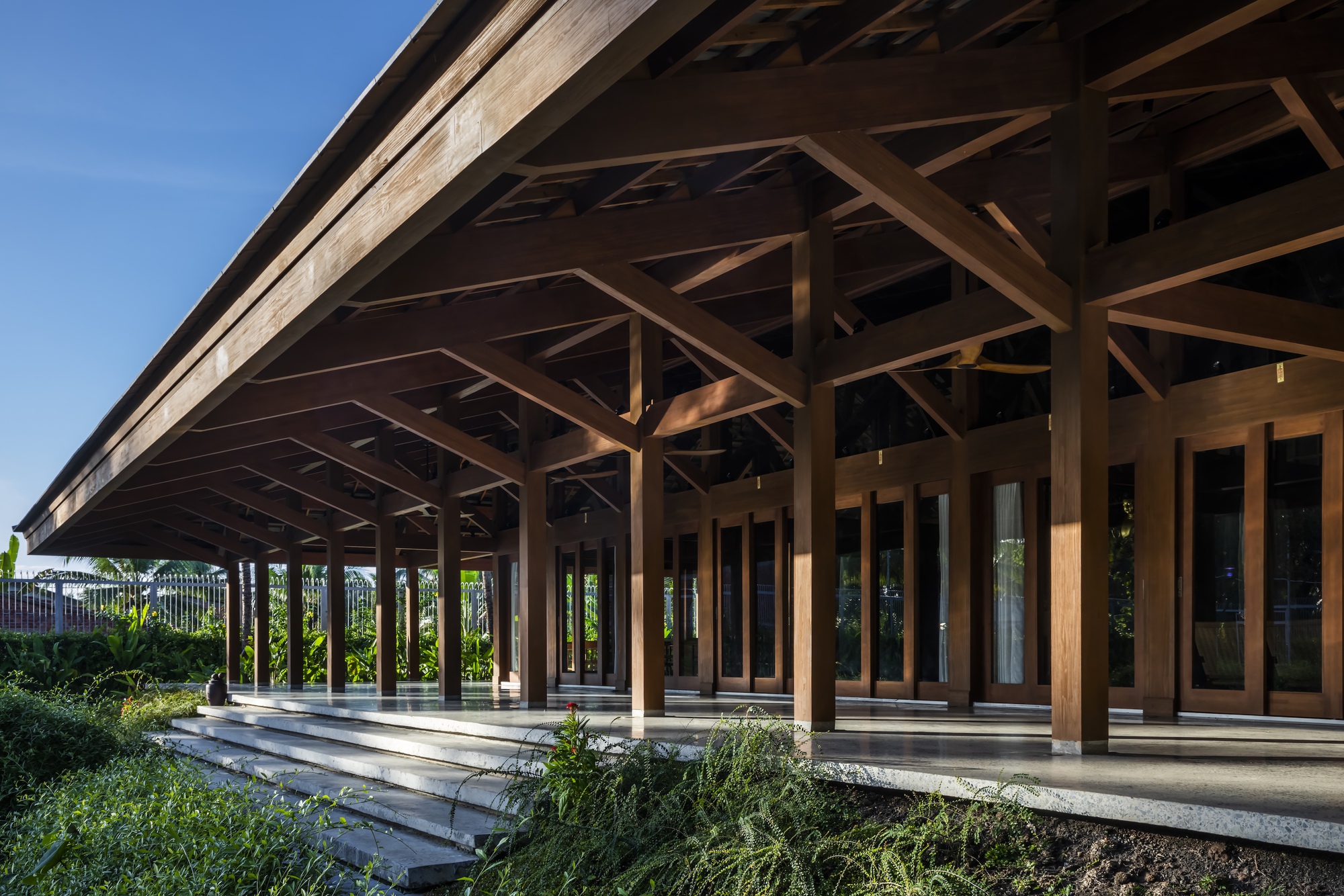 Exterior view of the deep eaves and timber columns along the planted edge under blue sky