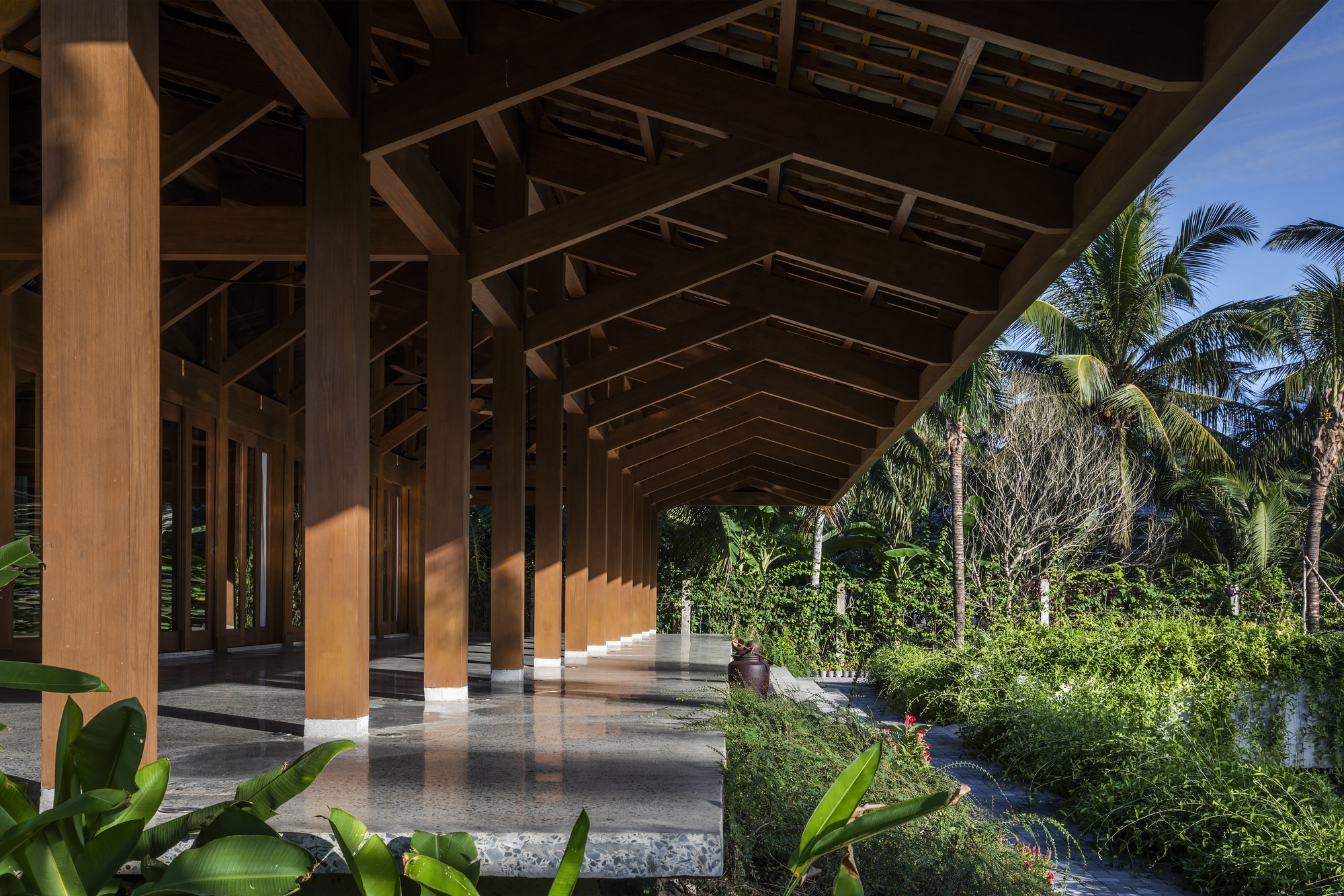 Covered terrace with timber structure and polished concrete floor overlooking palm trees