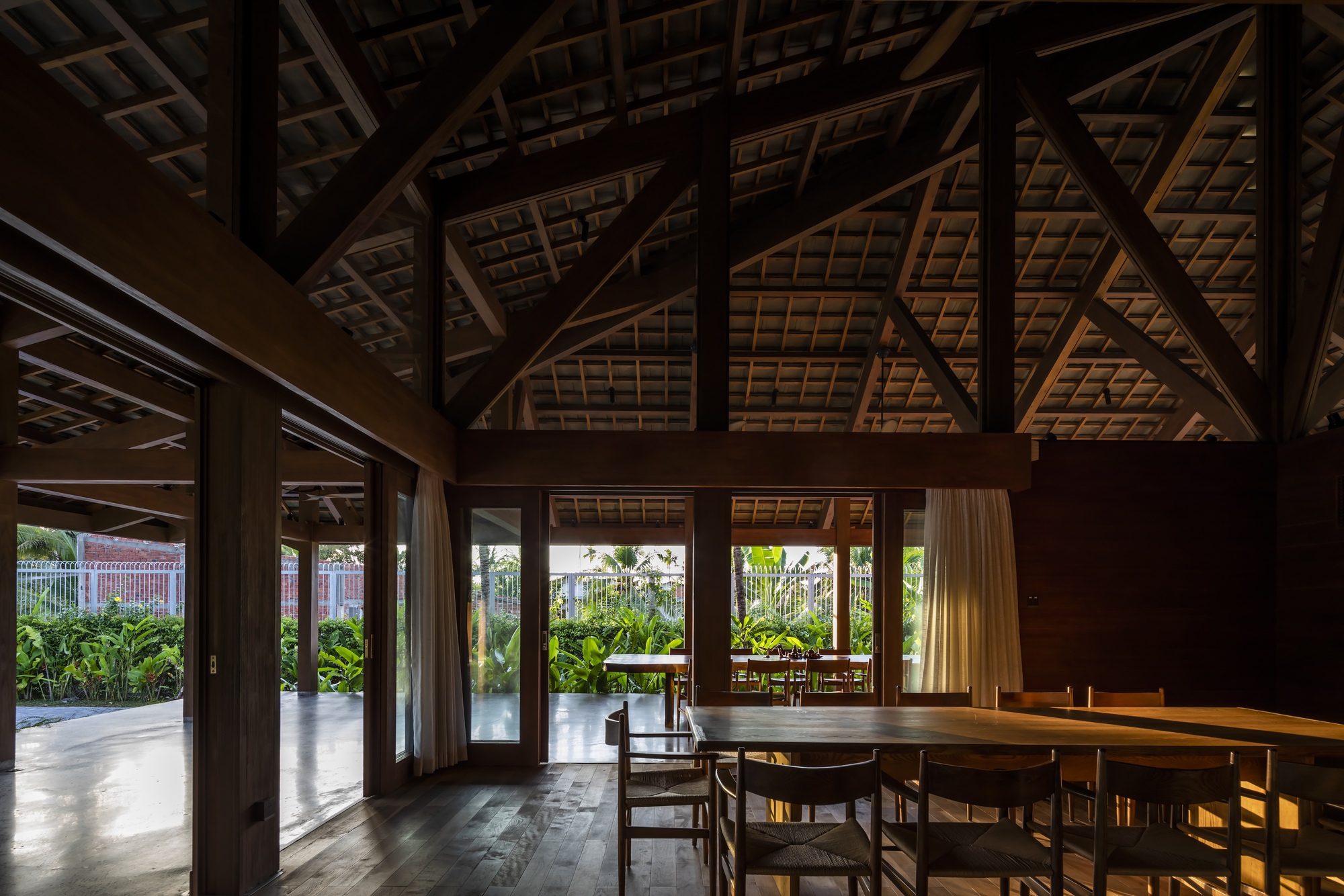 Dining space beneath exposed timber roof trusses with afternoon light filtering through glazed doors