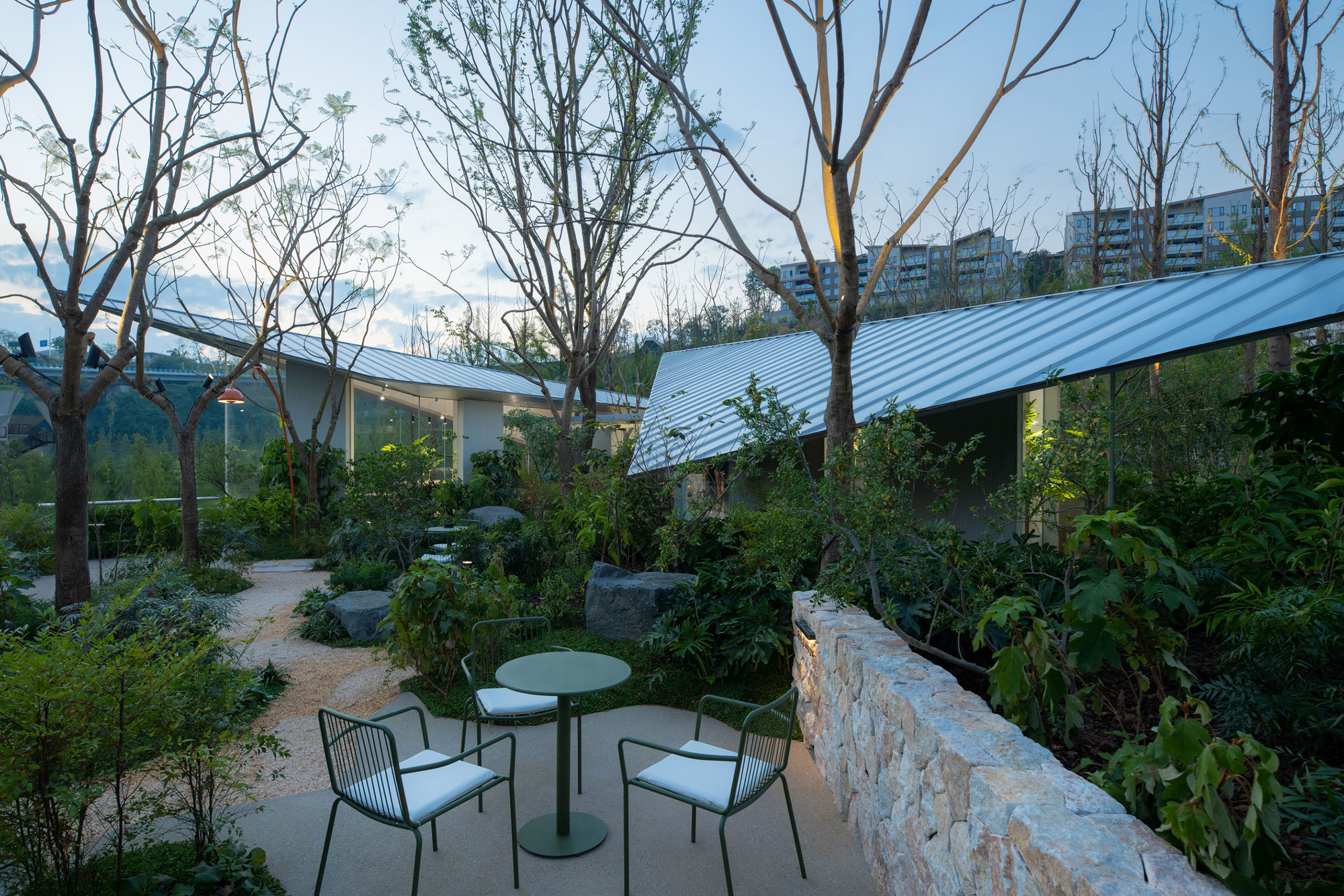 Courtyard seating area with stone retaining wall and corrugated metal roof visible beyond leafless trees